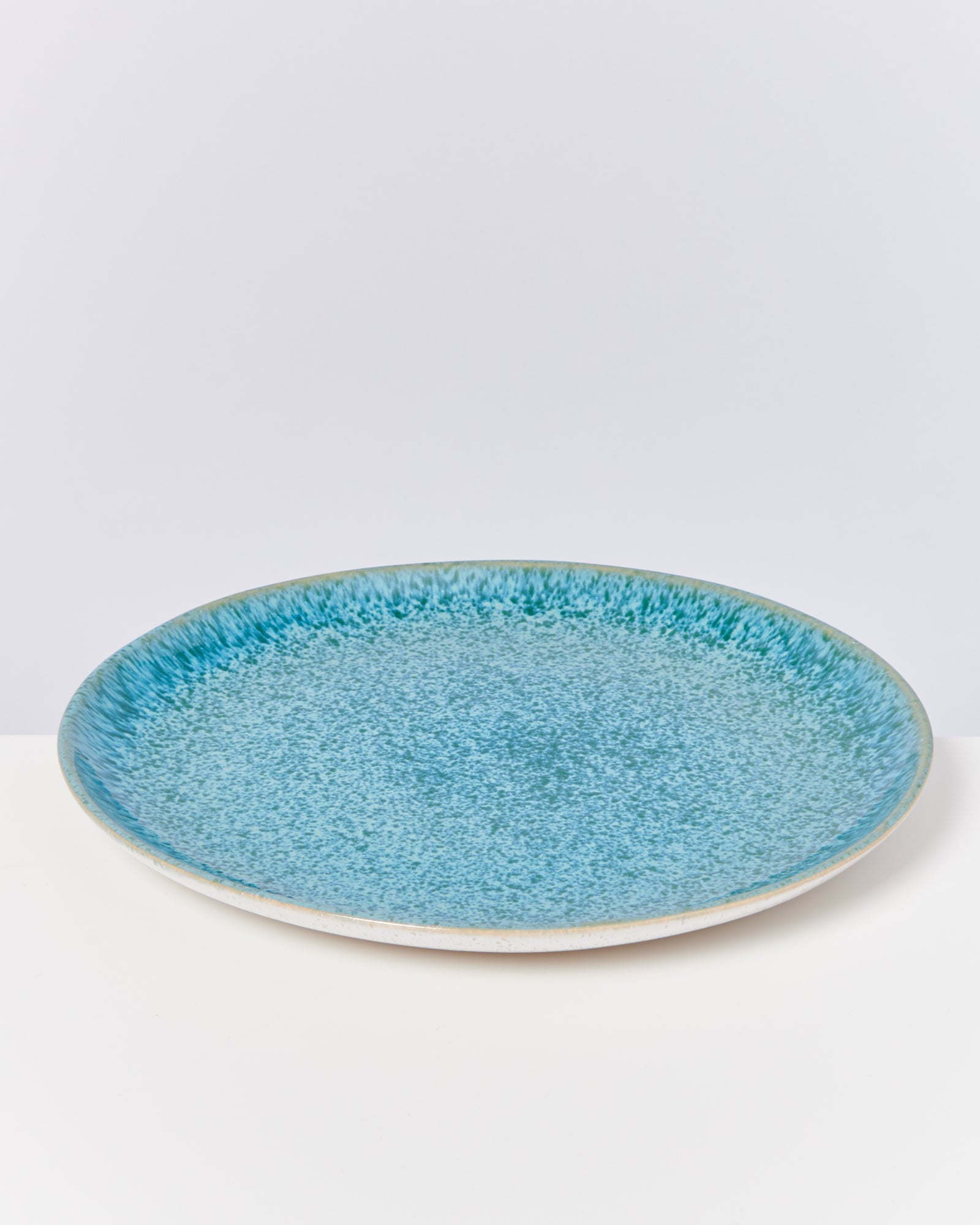 Flacher, runder Teller mit blau-grünem, geflecktem Design auf weißem Hintergrund.