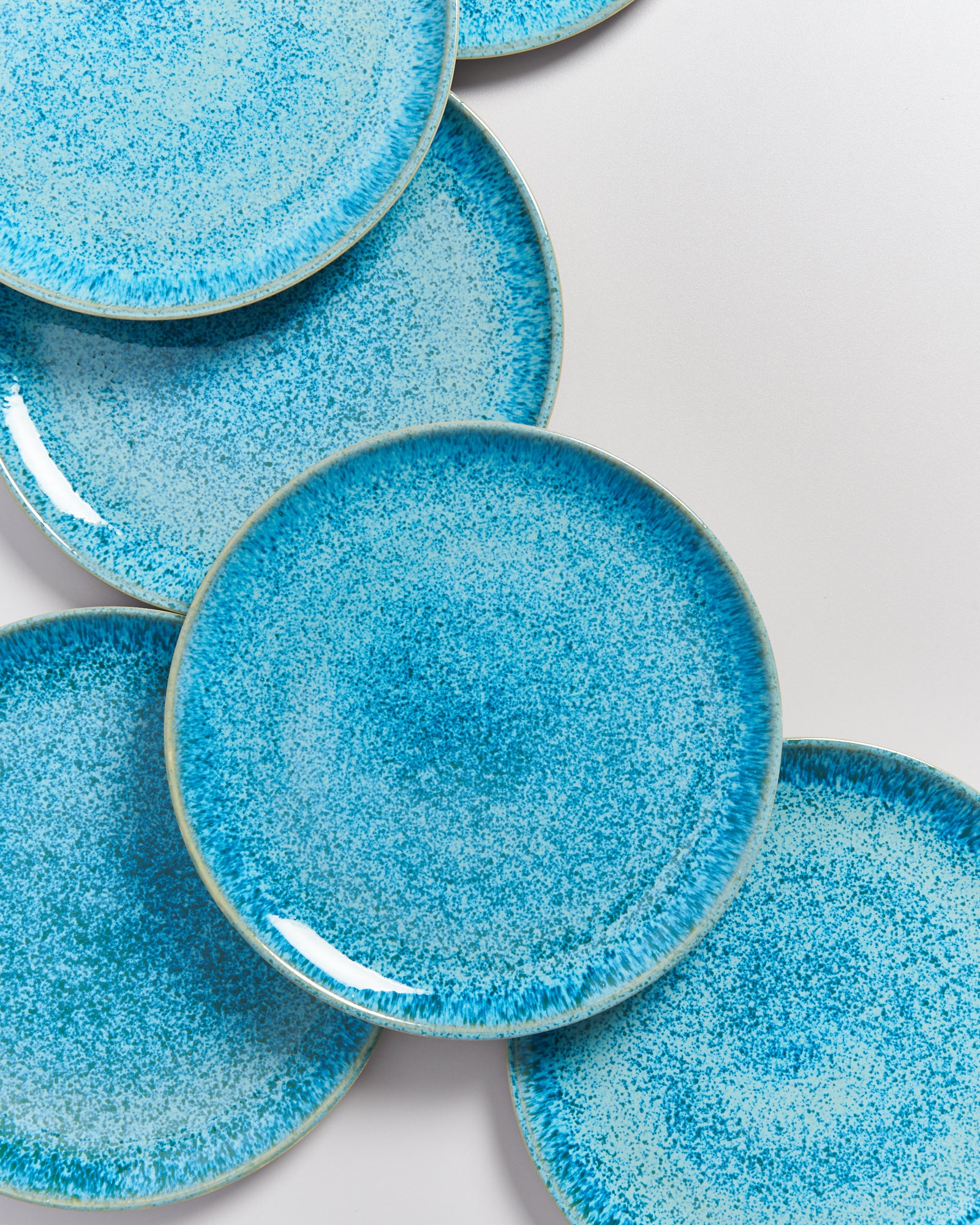 Sechs blaue, gesprenkelte Teller liegen überlappend auf einem weißen Hintergrund.