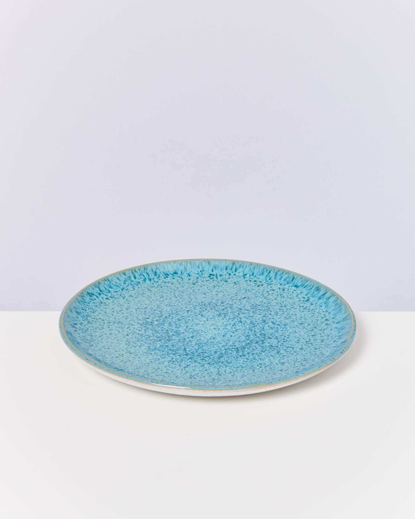 Ein runder, blauer Keramikteller mit gesprenkeltem Muster auf einer weißen Oberfläche.