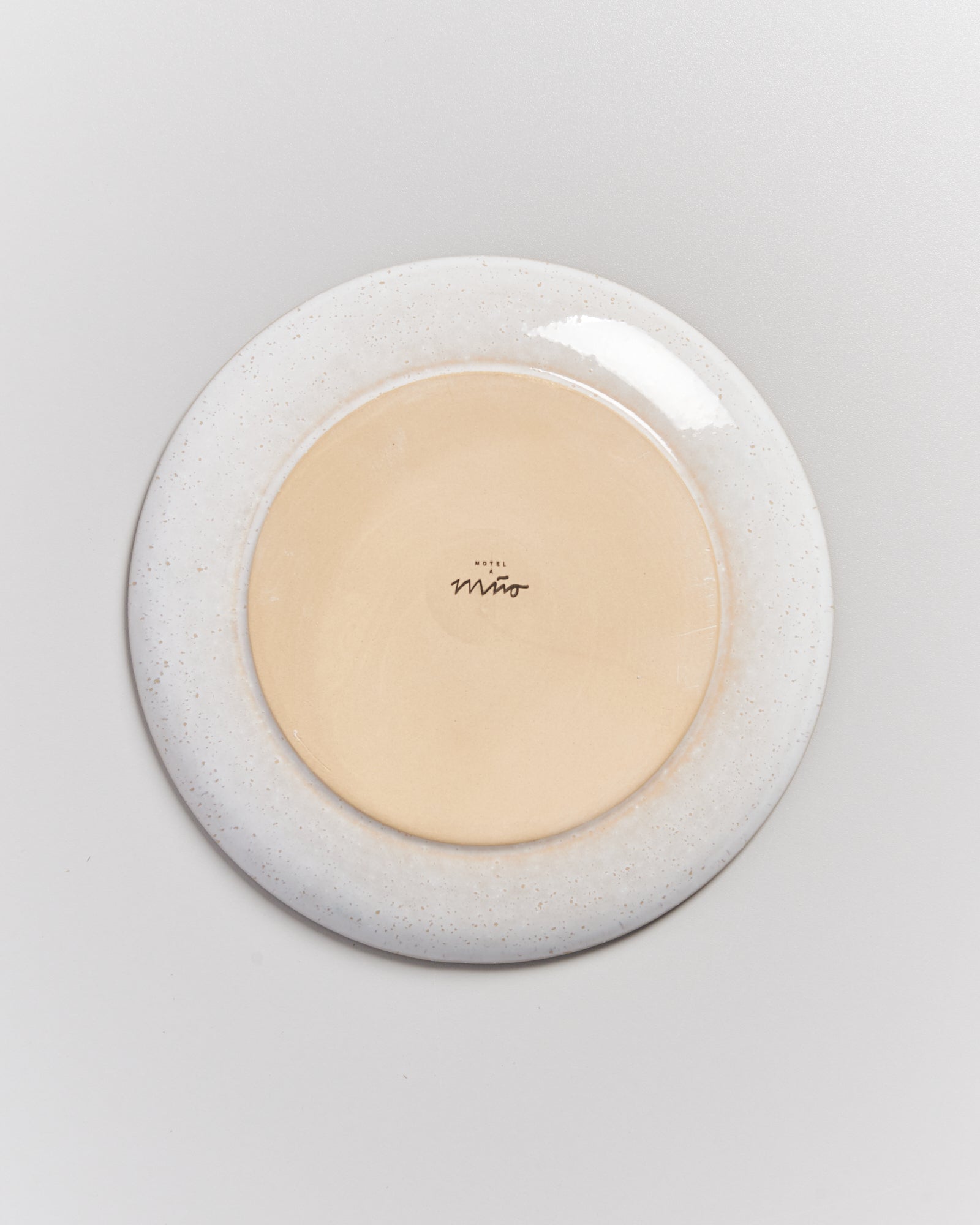 Die Unterseite eines Tellers mit dem Schriftzug "Hotel Miró" auf beigem Hintergrund, umgeben von einem weißen Rand.