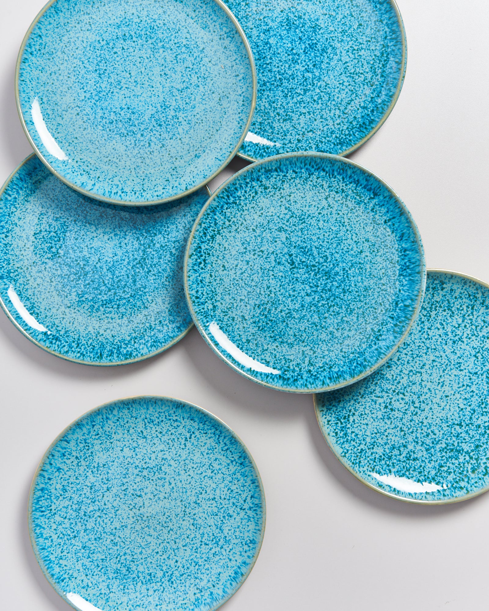 Sechs blaue gesprenkelte Teller auf einem weißen Hintergrund.