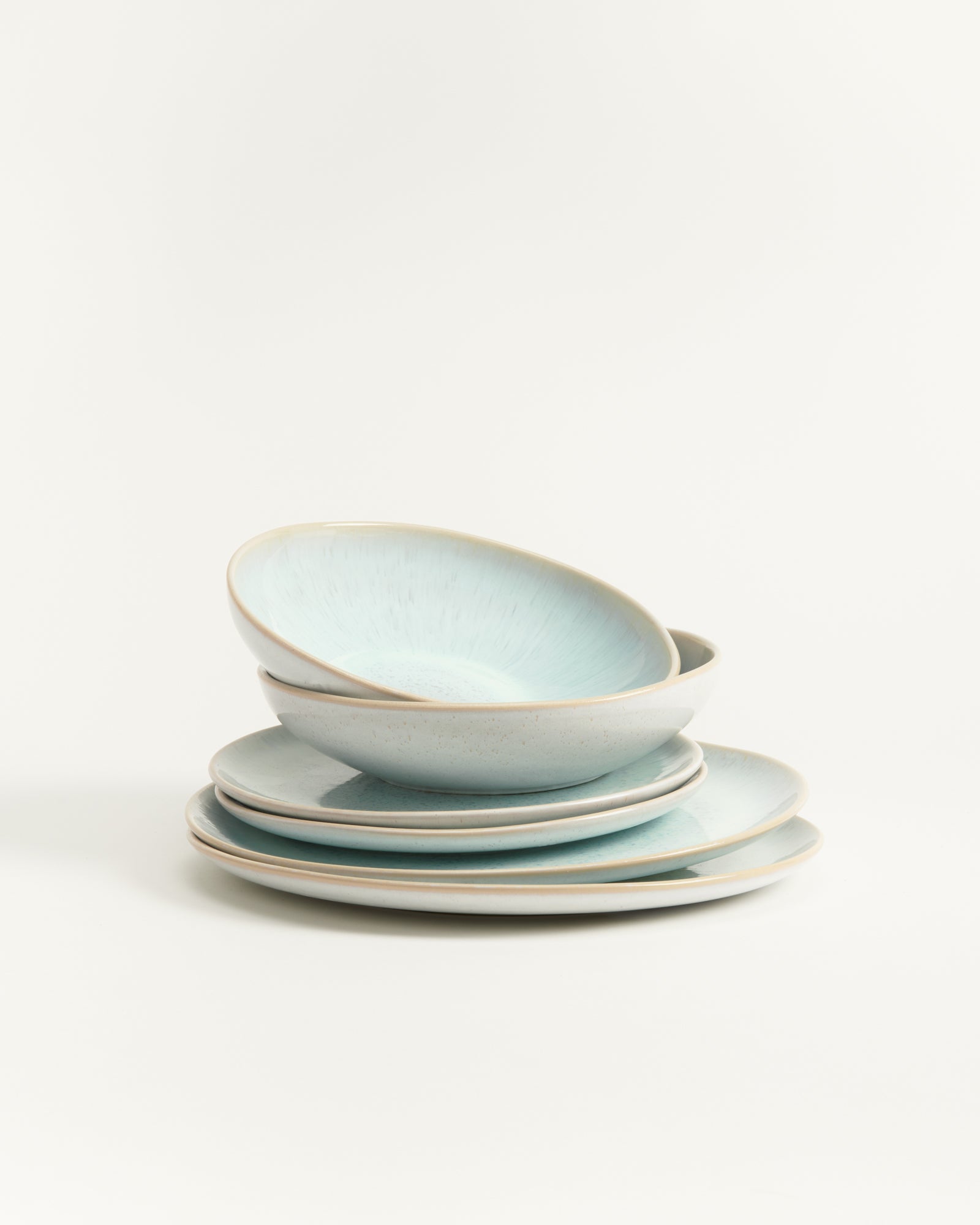 Ein Stapel aus hellblauen Keramiktellern und -schüsseln vor einem weißen Hintergrund.