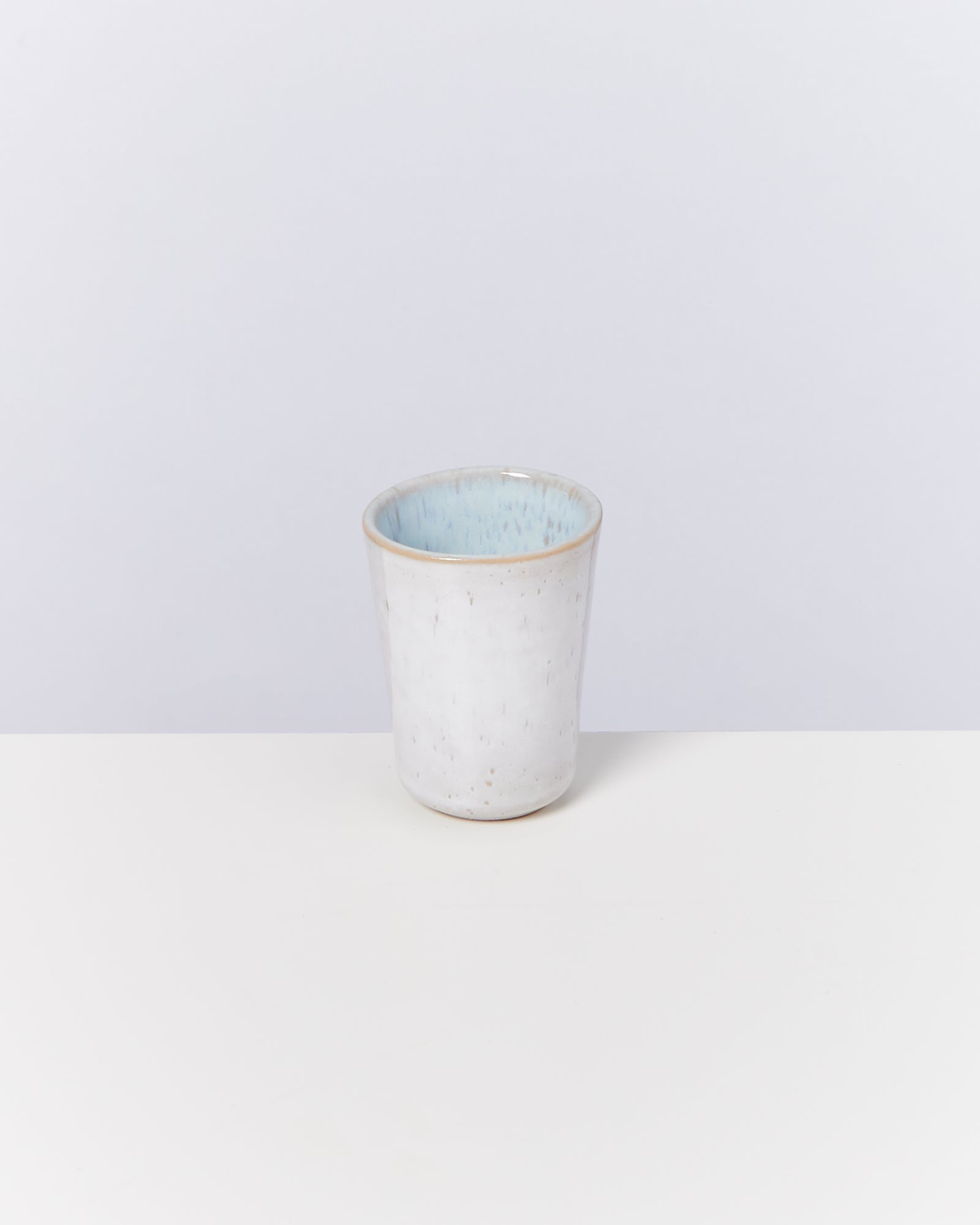 Weißer Keramikbecher mit blauer Innenseite, auf hellem Hintergrund platziert.