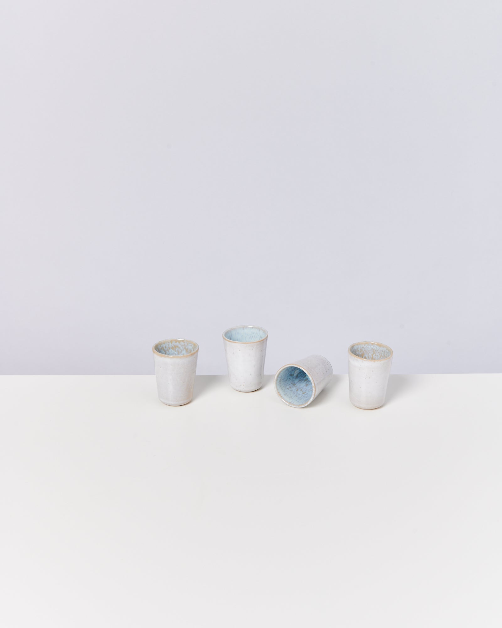 Vier weiße, zylindrische Becher, einer liegend, auf einer weißen Oberfläche vor einem hellgrauen Hintergrund.