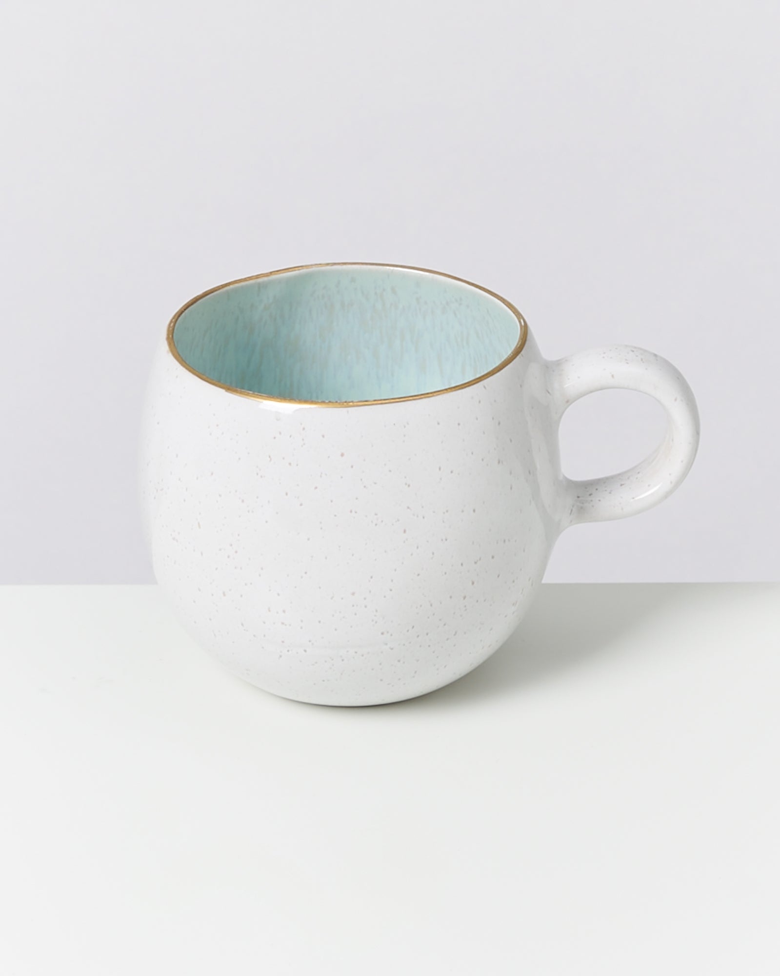 Weiße Keramiktasse mit blauem Inneren und goldener Kante auf weißem Hintergrund.