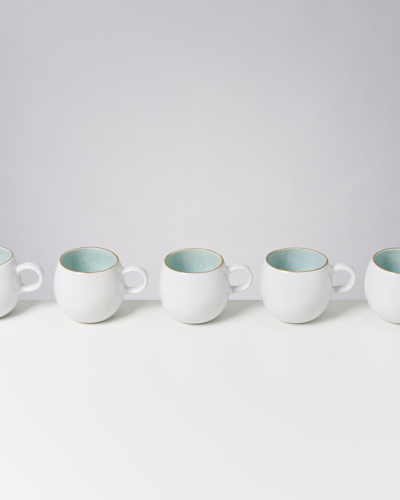 Fünf weiße Tassen mit türkisfarbigem Inneren in einer Reihe auf einem weißen Hintergrund.