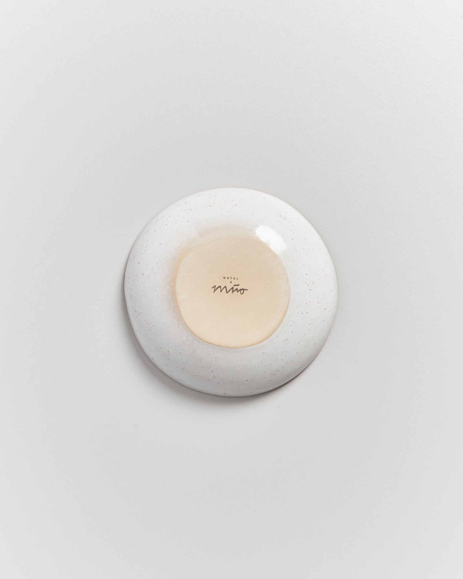 Runde, weiße Keramikplatte von unten, mit der Aufschrift "Hotel Miro" in der Mitte, auf hellem Hintergrund.
