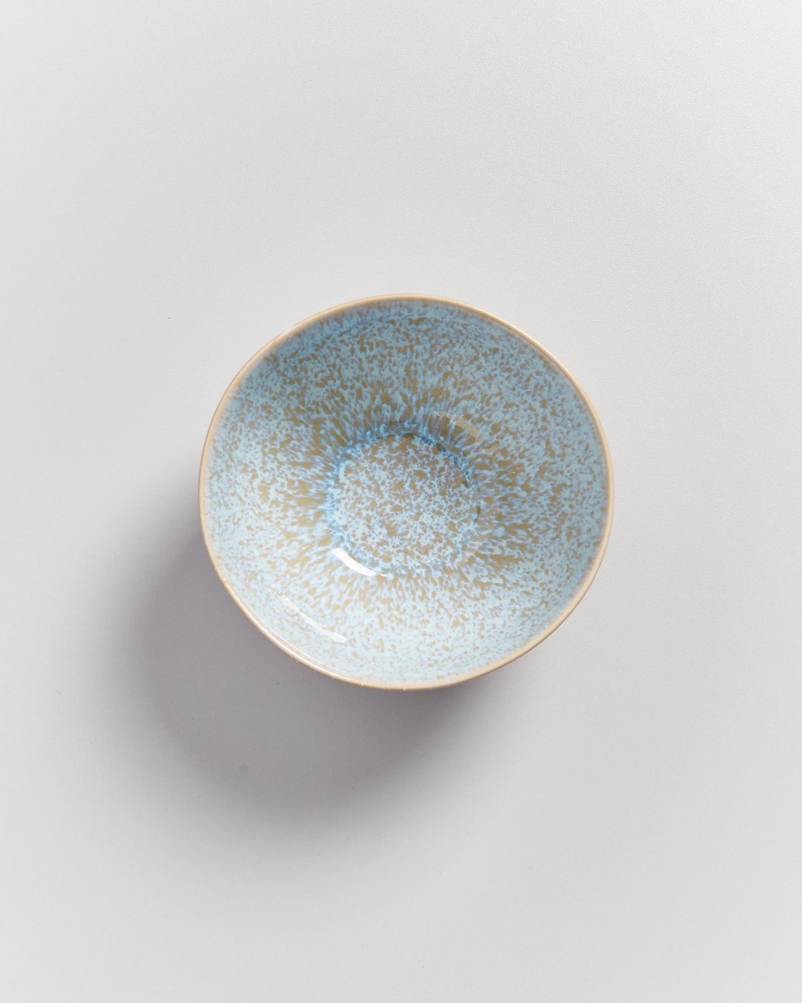 Keramikschale mit blauen und beige gesprenkelten Mustern auf heller Oberfläche.