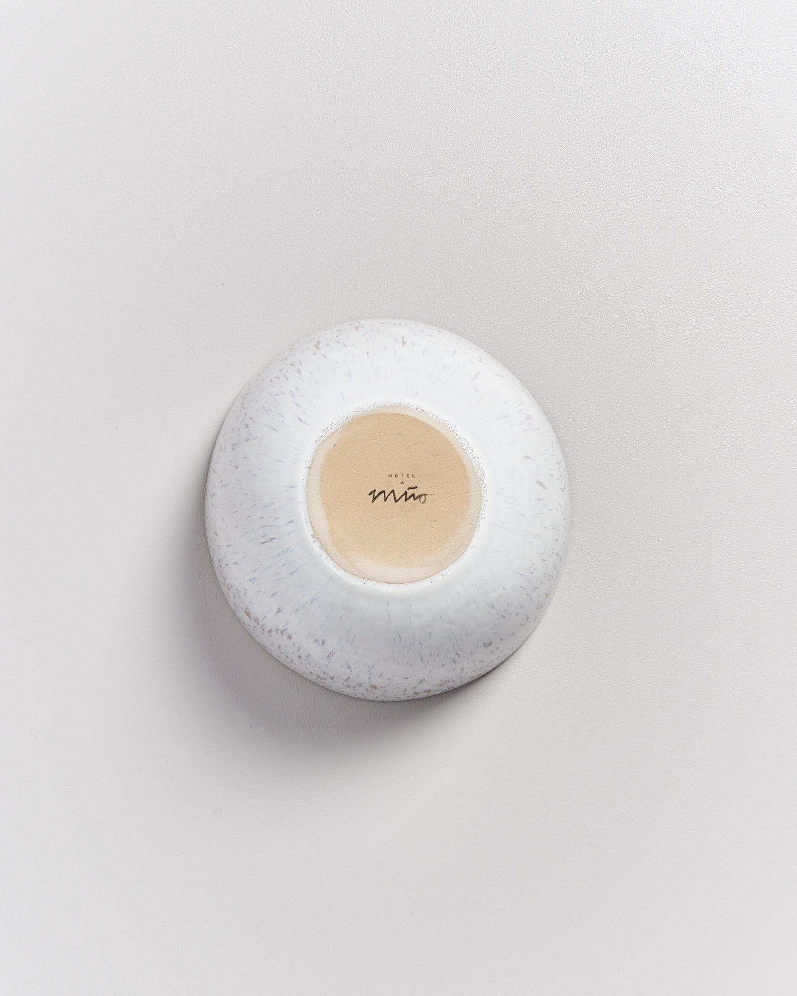 Weiße, runde Unterseite einer Tasse mit dem Aufdruck "Hotel Miró" auf hellem Hintergrund.