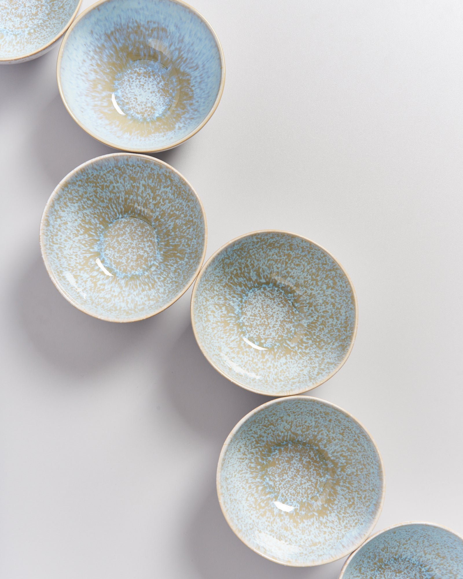 Sechs blaue, gesprenkelte Schalen sind diagonal auf einer weißen Oberfläche angeordnet.