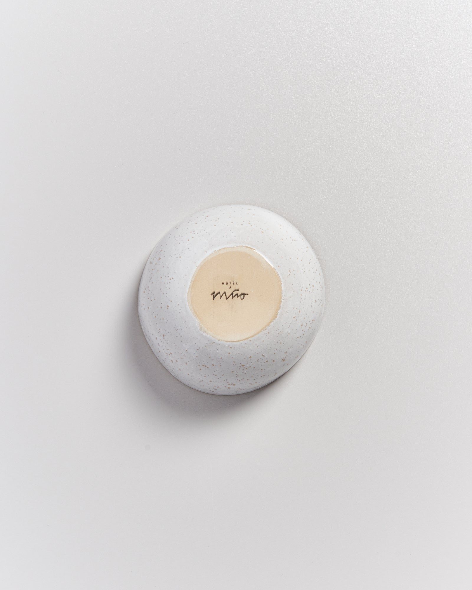 Weiße, runde Keramikschale mit beiger Innenseite und schwarzem Schriftzug in der Mitte der Unterseite auf hellem Hintergrund.