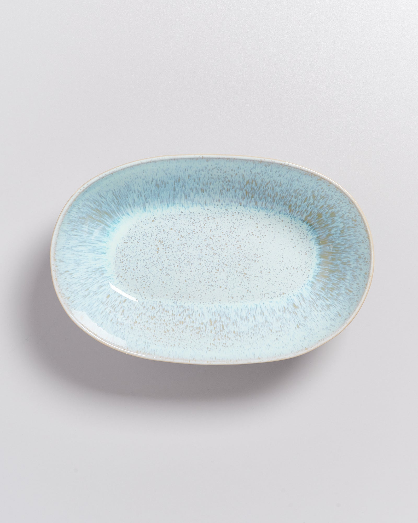 Ein ovaler, hellblauer Keramikteller mit gesprenkeltem Muster vor einem weißen Hintergrund.