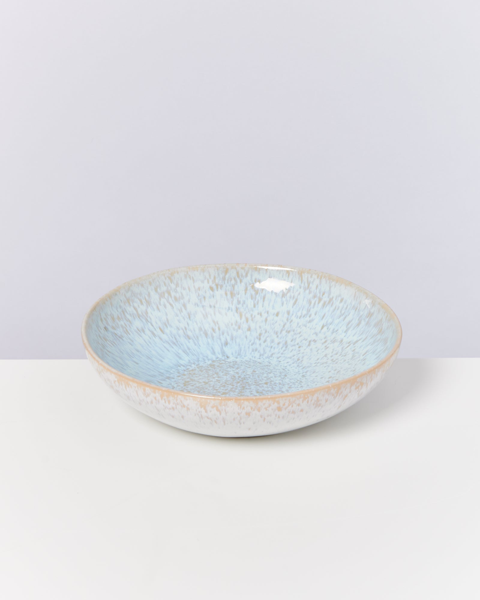 Keramikschale mit blauer und beiger Sprenkelglasur auf weißem Hintergrund.