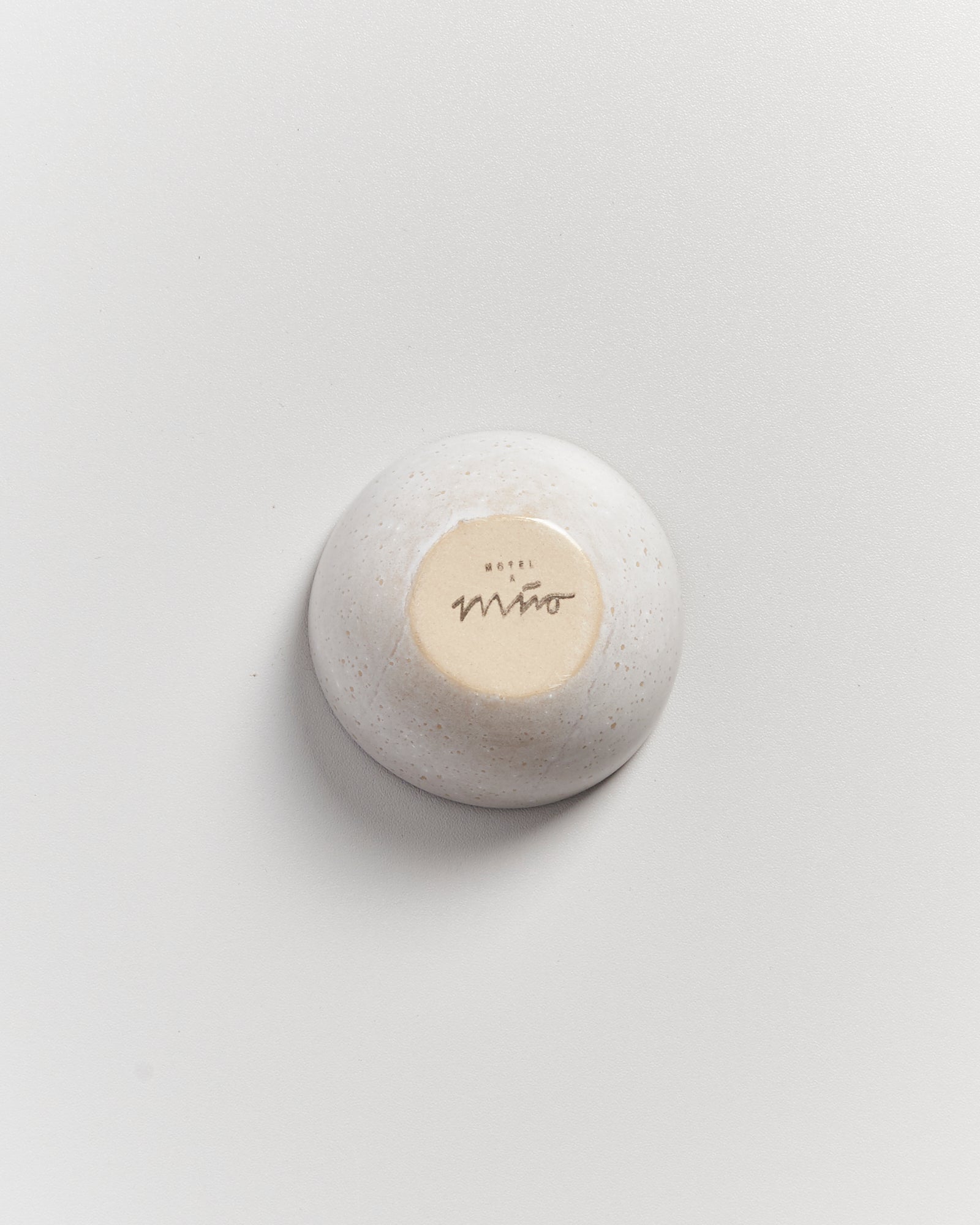 Eine umgedrehte, weiße Keramikschale mit dem Schriftzug "Hotel Mito" auf einem hellen Hintergrund.