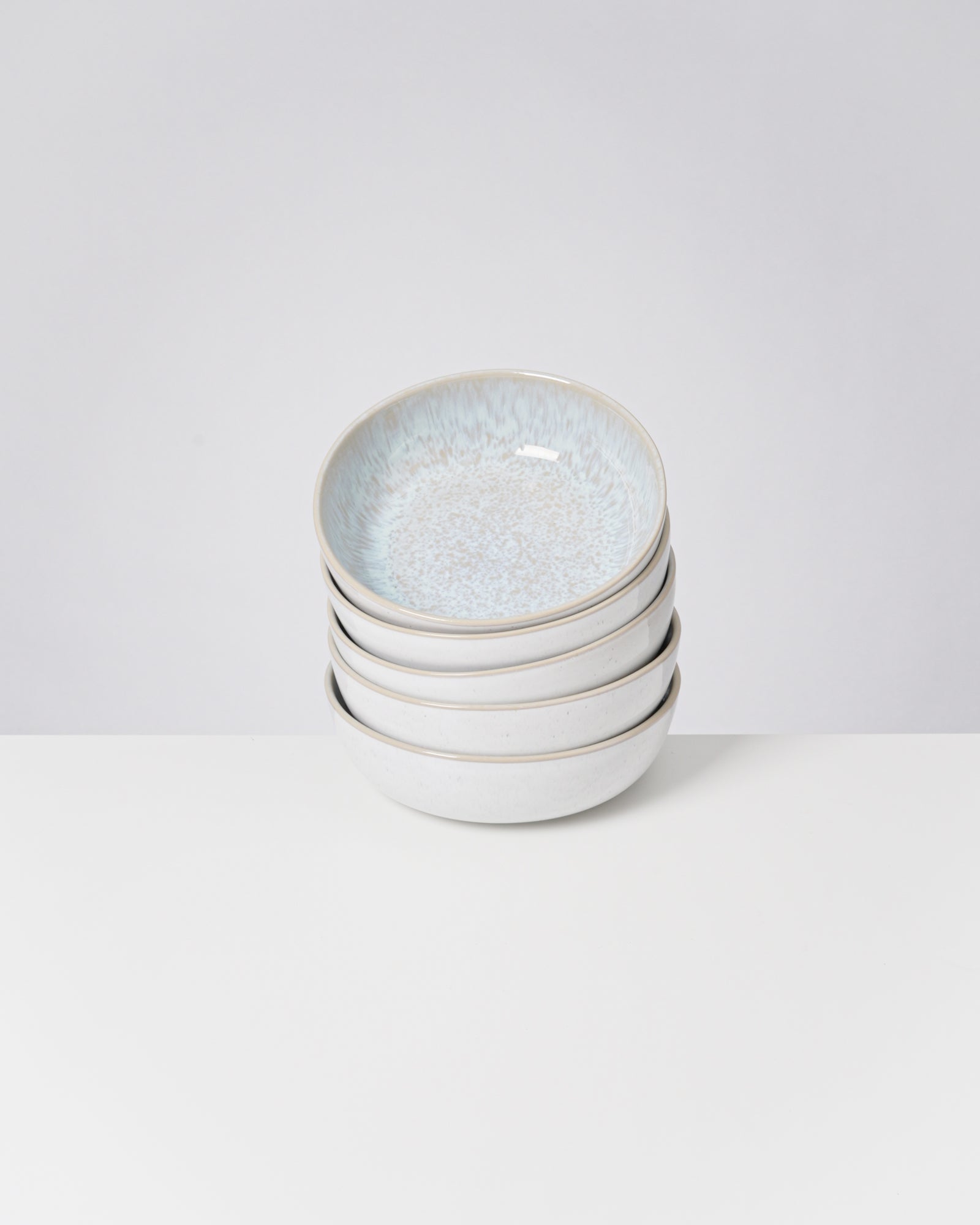 Ein Stapel von vier weißen Keramikschalen mit einem hellblauen Muster auf einem weißen Hintergrund.