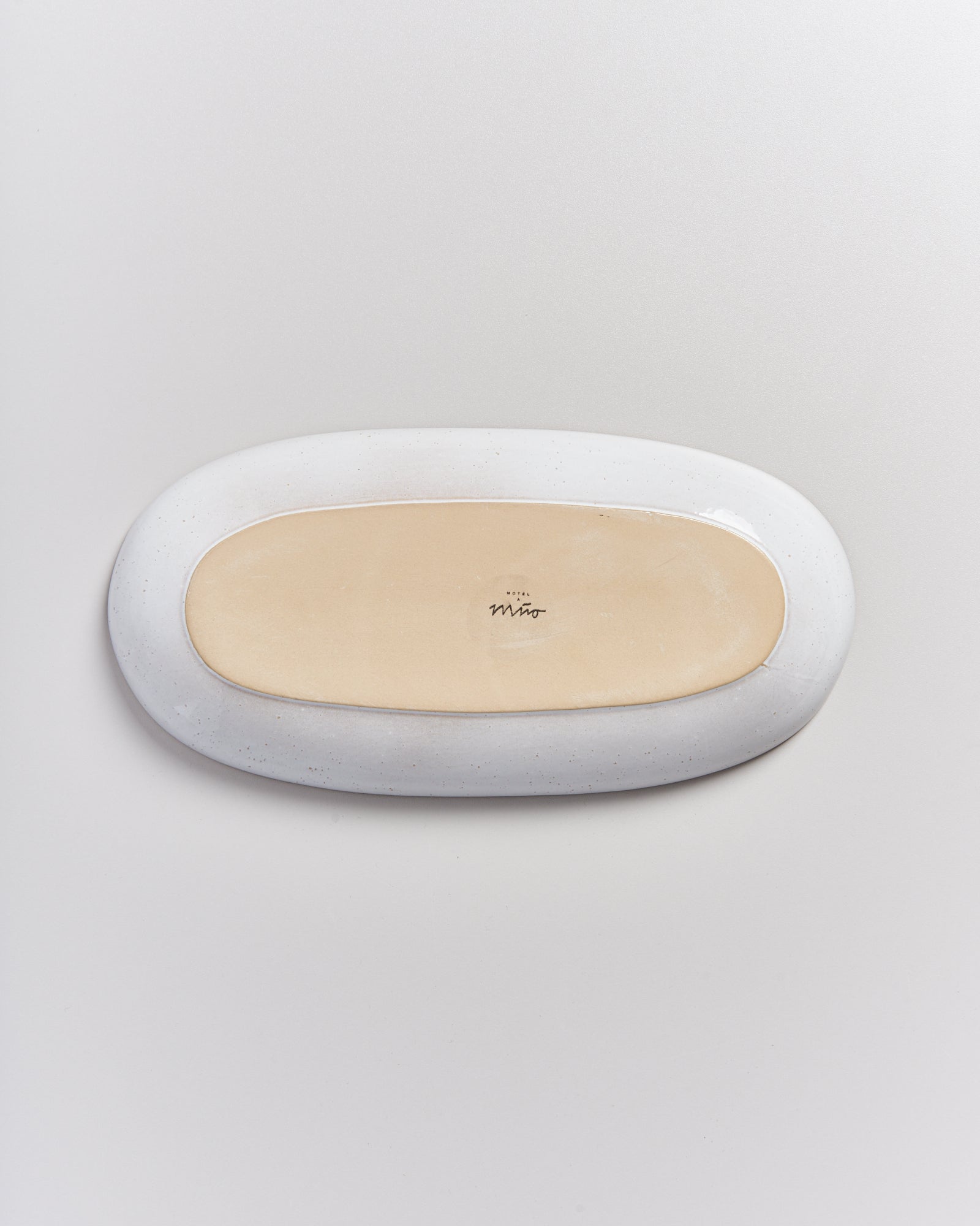 Ovaler Keramikteller mit hellbraunem Zentrum und weißem Rand, auf einer hellen Oberfläche liegend.