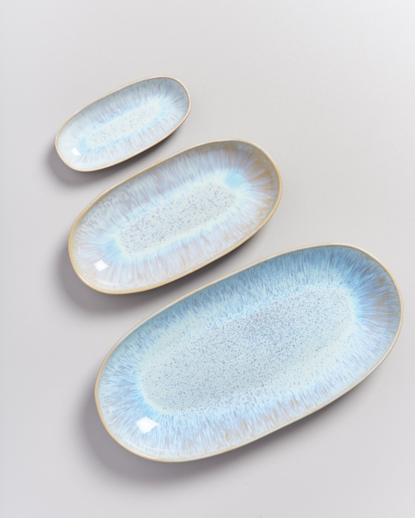 Drei ovale Teller in verschiedenen Größen mit blauen und beigen Mustern liegen auf einer weißen Oberfläche.