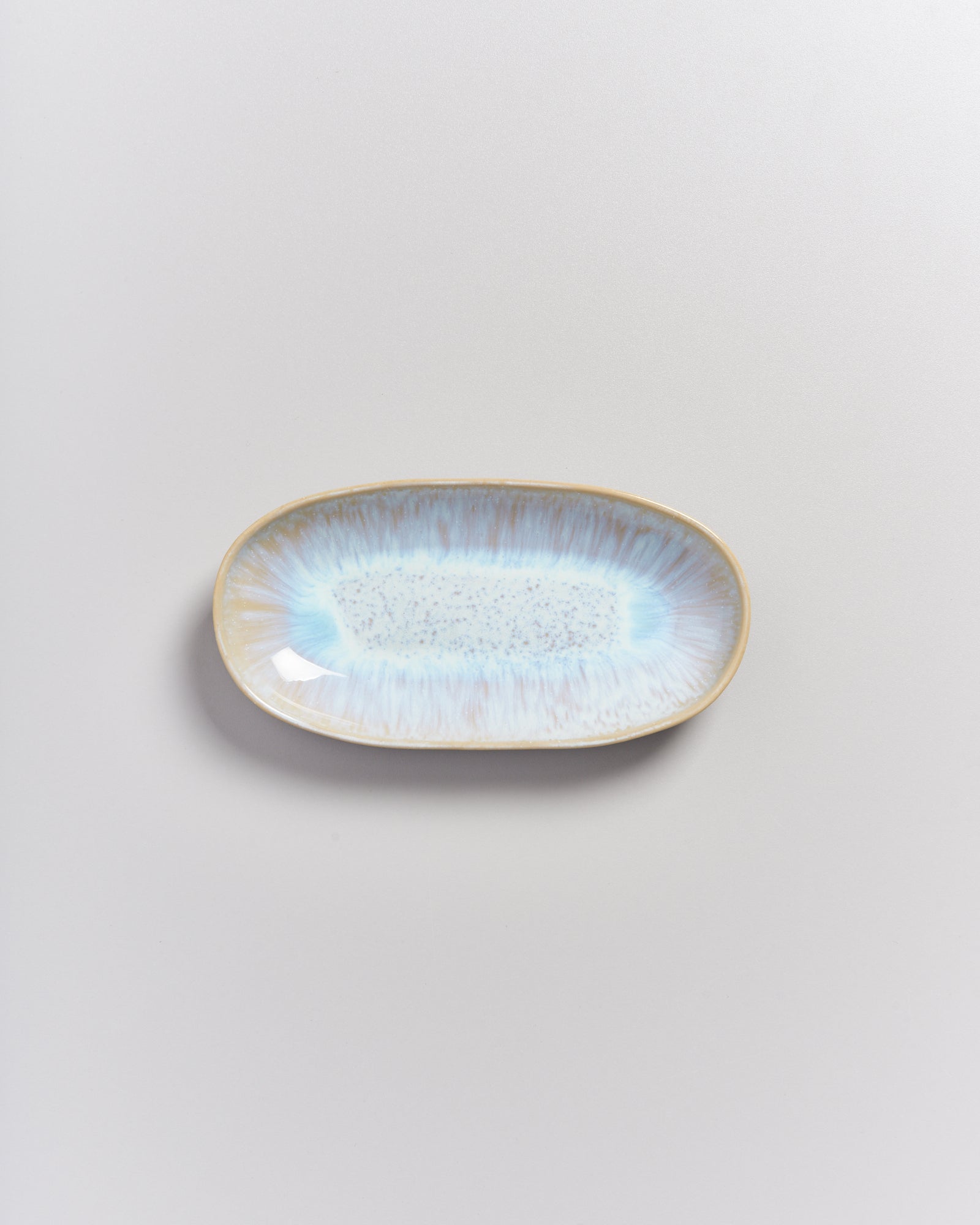 Ovale, hellblaue Keramikschale mit braunem Rand auf hellem Hintergrund.