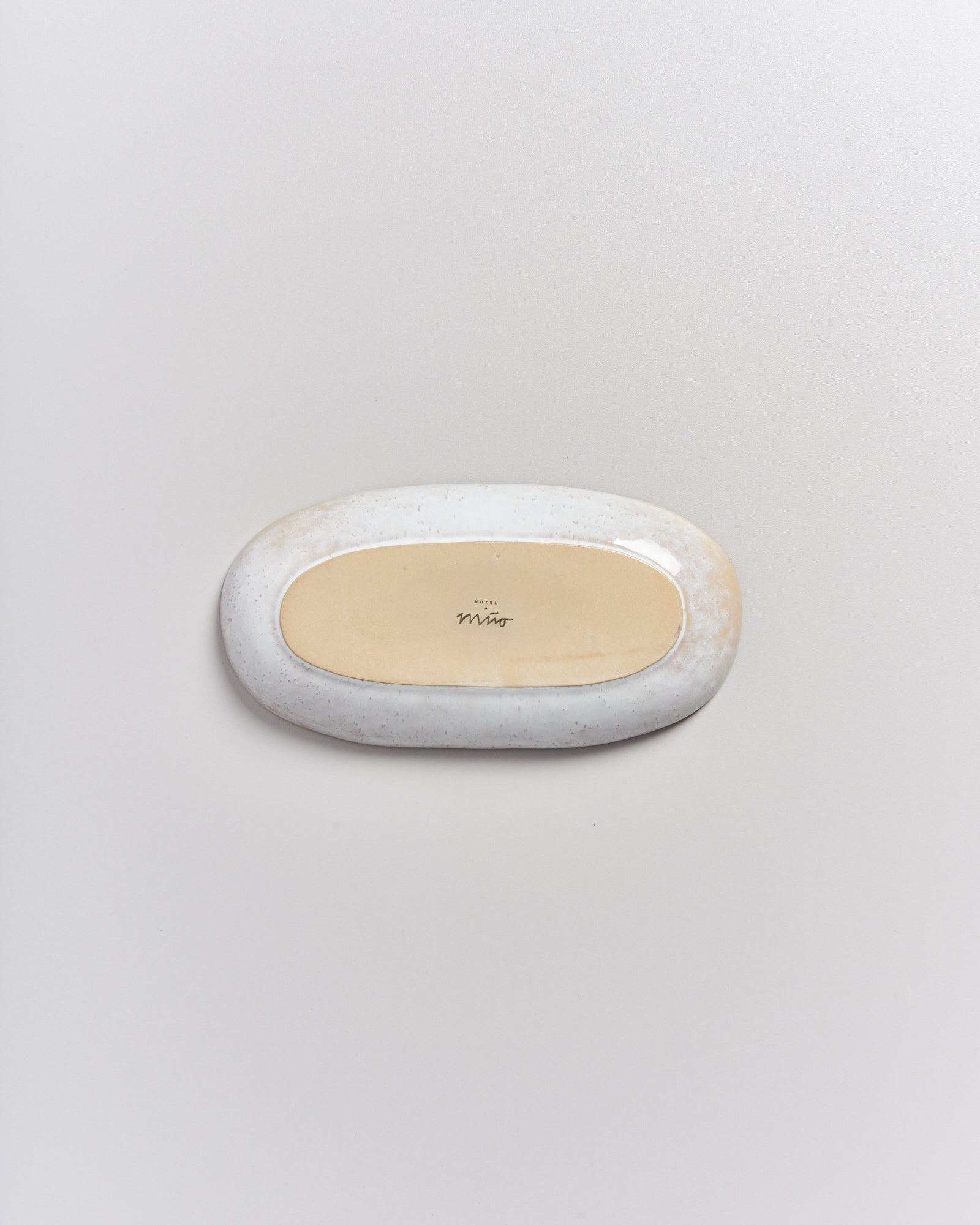 Ovaler Keramikteller mit hellbraunem Boden und weißem Rand, auf grauem Hintergrund.