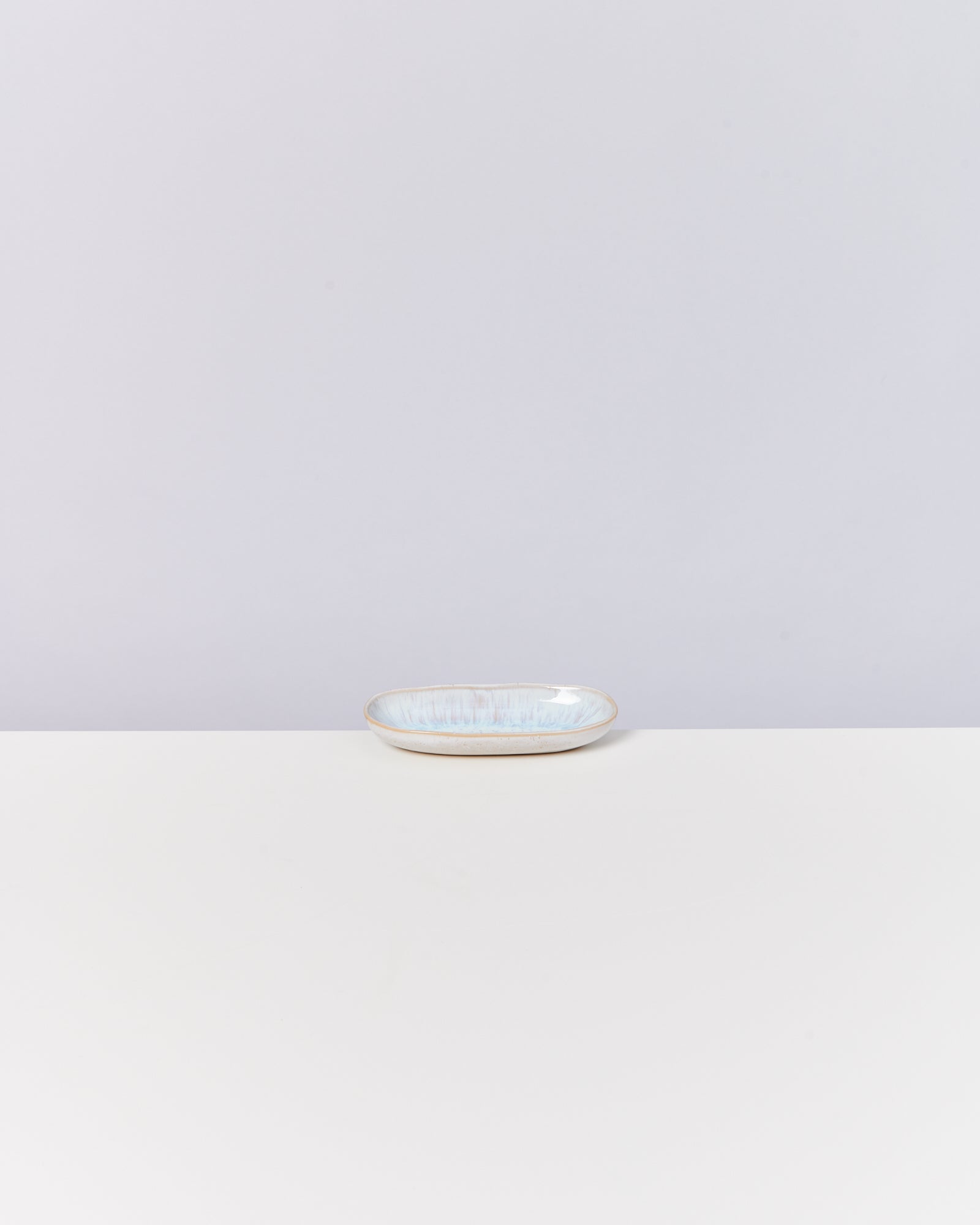 Kleiner, ovaler Keramikteller auf weißem Tisch vor grauem Hintergrund.
