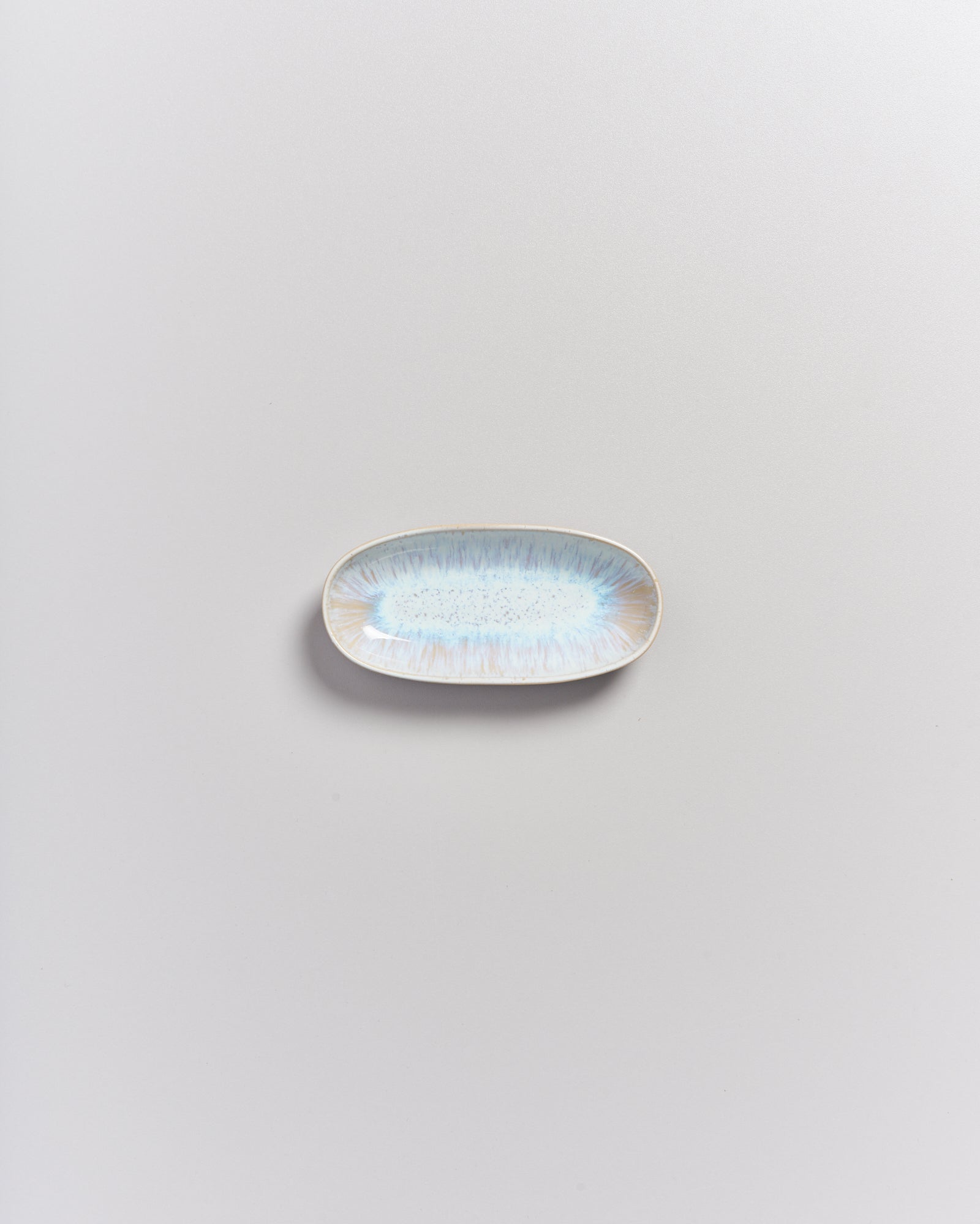 Kleiner ovaler Keramikteller mit blau-braunem Muster auf weißem Hintergrund.