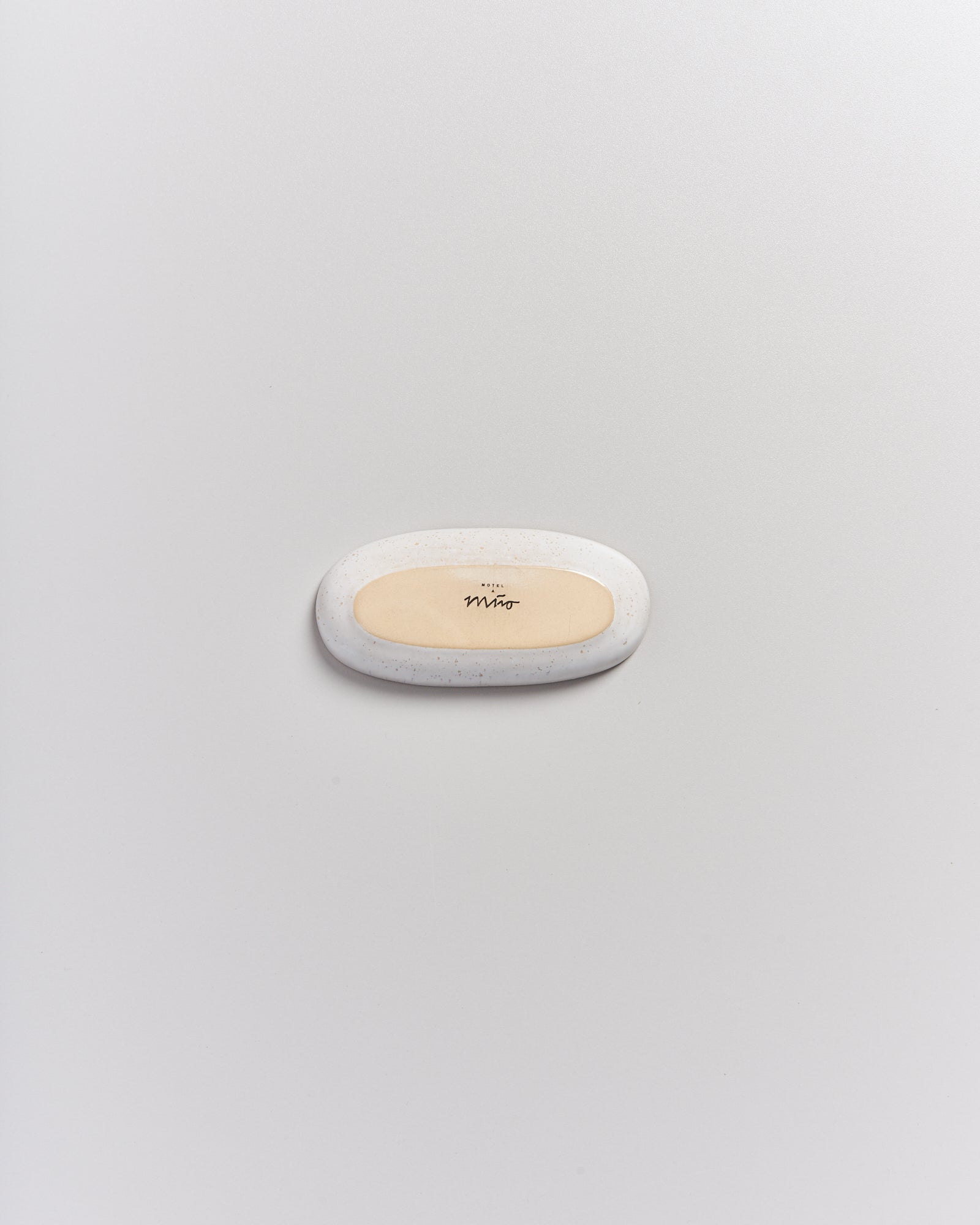 Eine ovale, cremefarbene Seife mit der Aufschrift "Mino" liegt auf einer weißen, glatten Oberfläche.