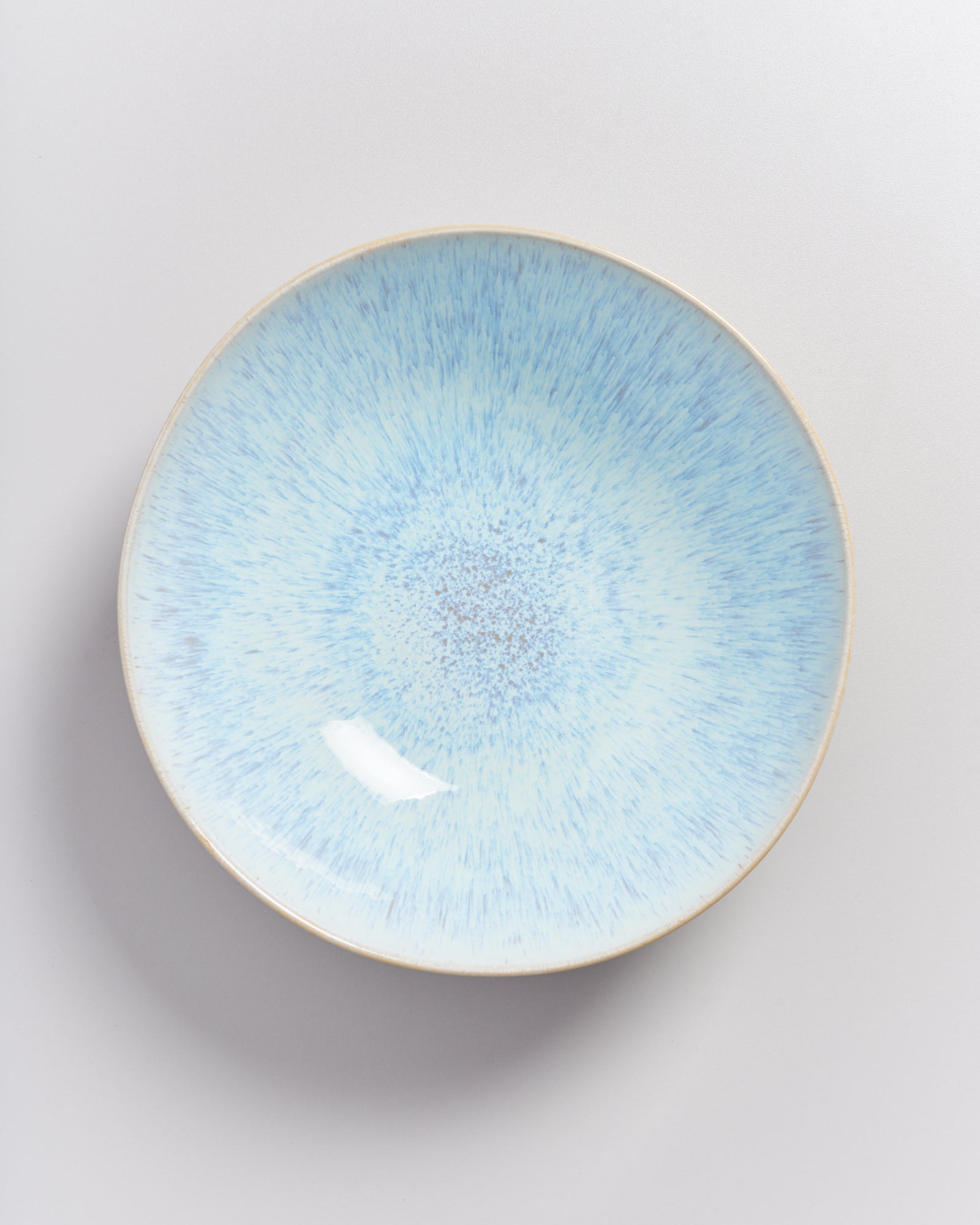 Ein runder Teller mit blauer, gesprenkelter Glasur auf weißem Hintergrund.