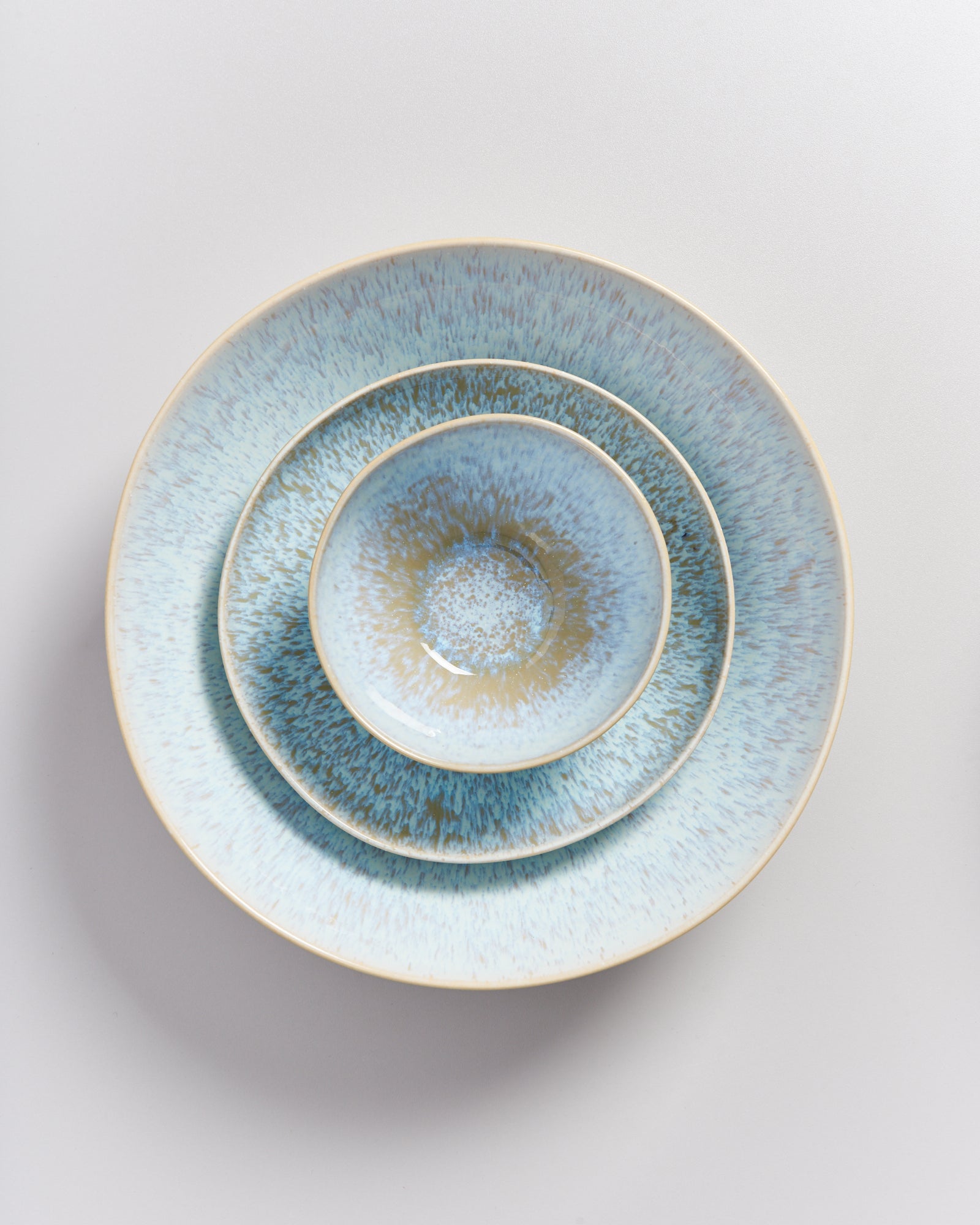 Drei ineinander gestapelte blaue Teller mit gesprenkeltem Muster auf weißem Hintergrund.