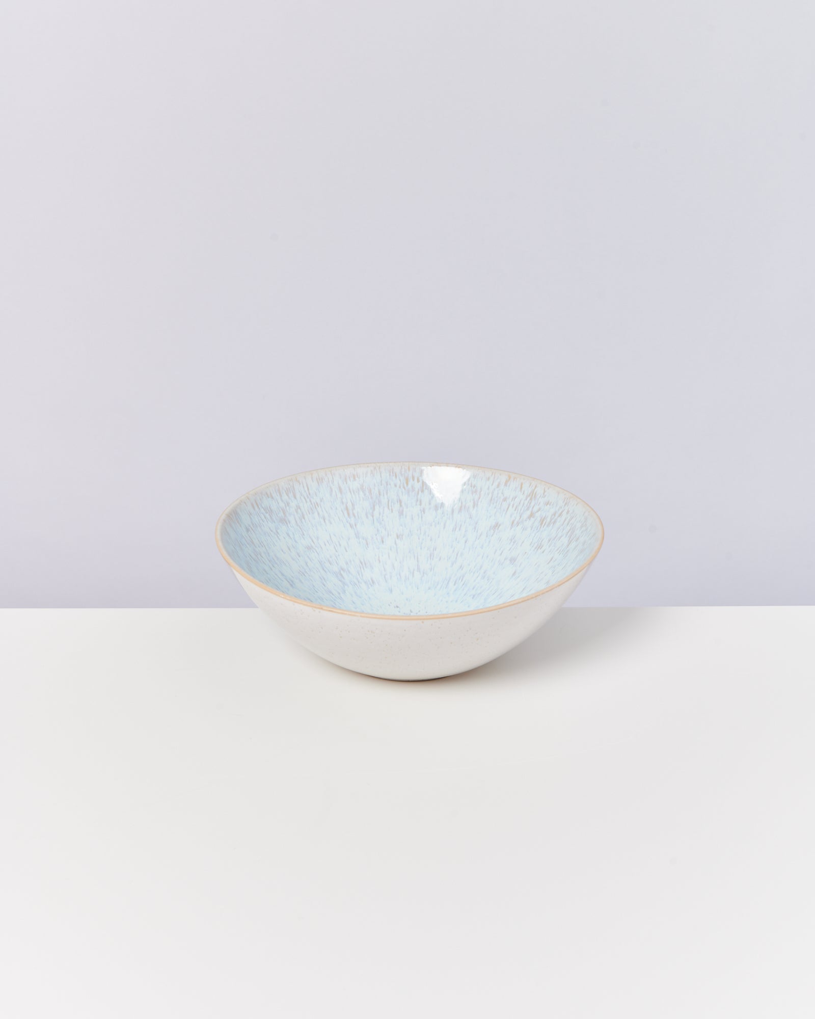 Eine helle Keramikschüssel mit bläulichem Muster steht auf einem weißen Tisch vor einer grauen Wand.
