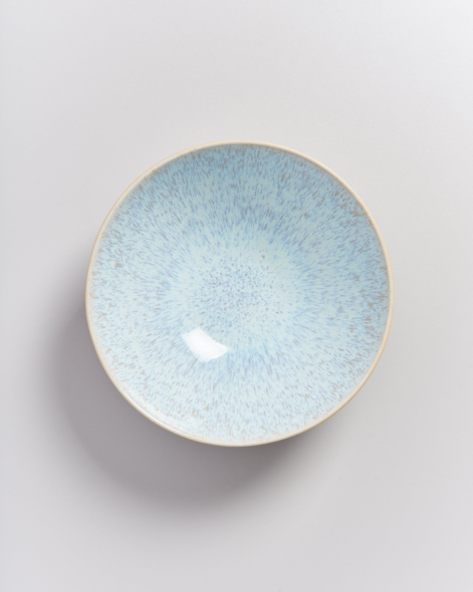 Eine runde, hellblaue Keramikschale mit gesprenkeltem Muster auf hellem Hintergrund.