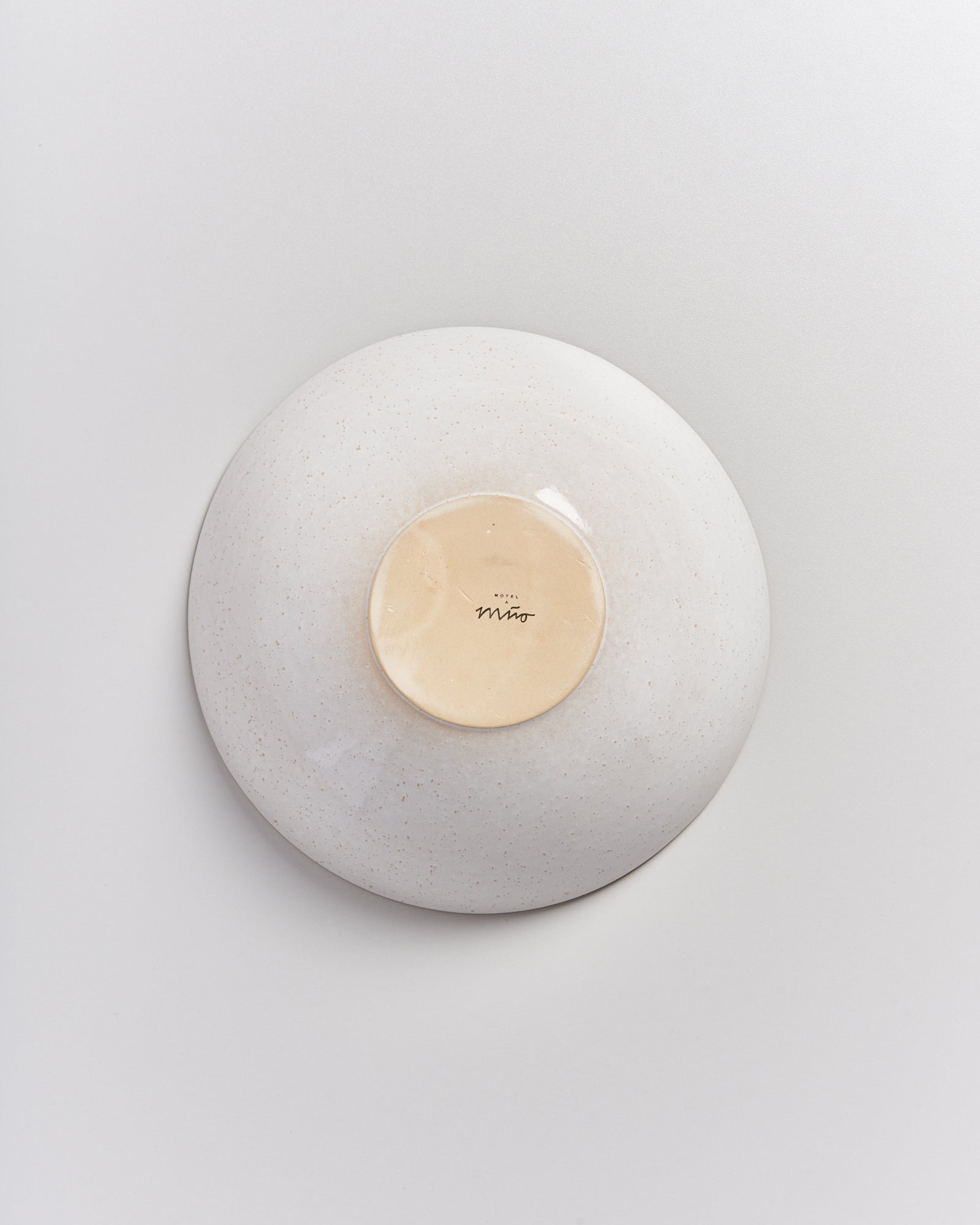 Die Unterseite einer weißen Keramikschale mit heller, glatter Mitte und dem Aufdruck "Miro" auf einem hellen Hintergrund.
