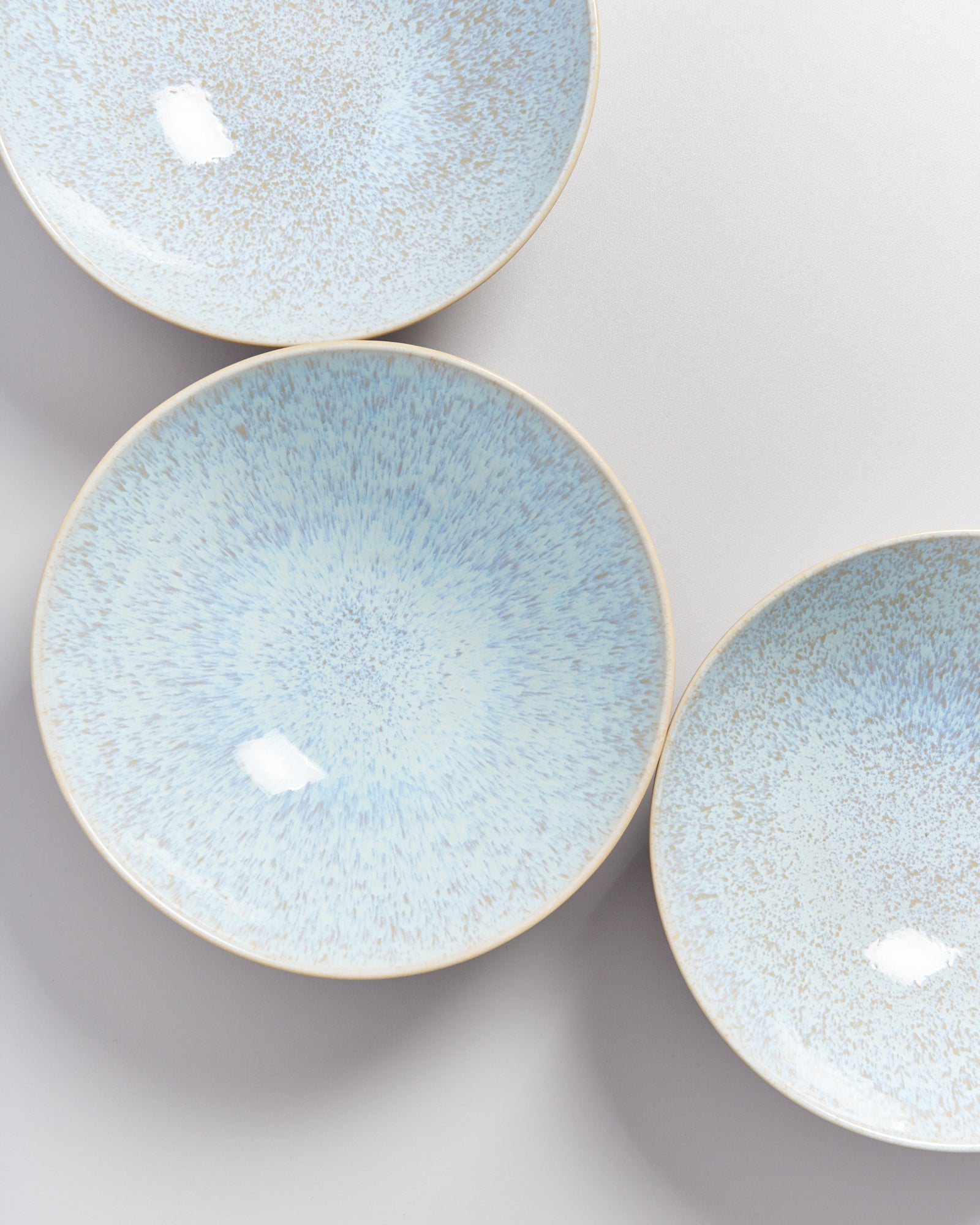 Drei blau-weiß gesprenkelte Teller liegen teils überlappend auf einer weißen Oberfläche.