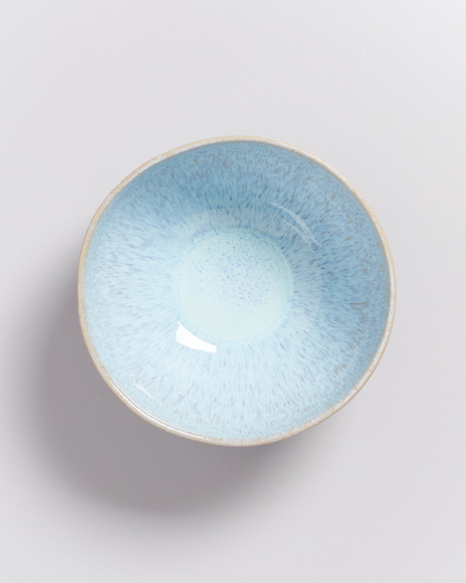 Blaue Keramikschale mit glasiertem, gesprenkeltem Inneren und rauem Rand auf hellem Hintergrund.