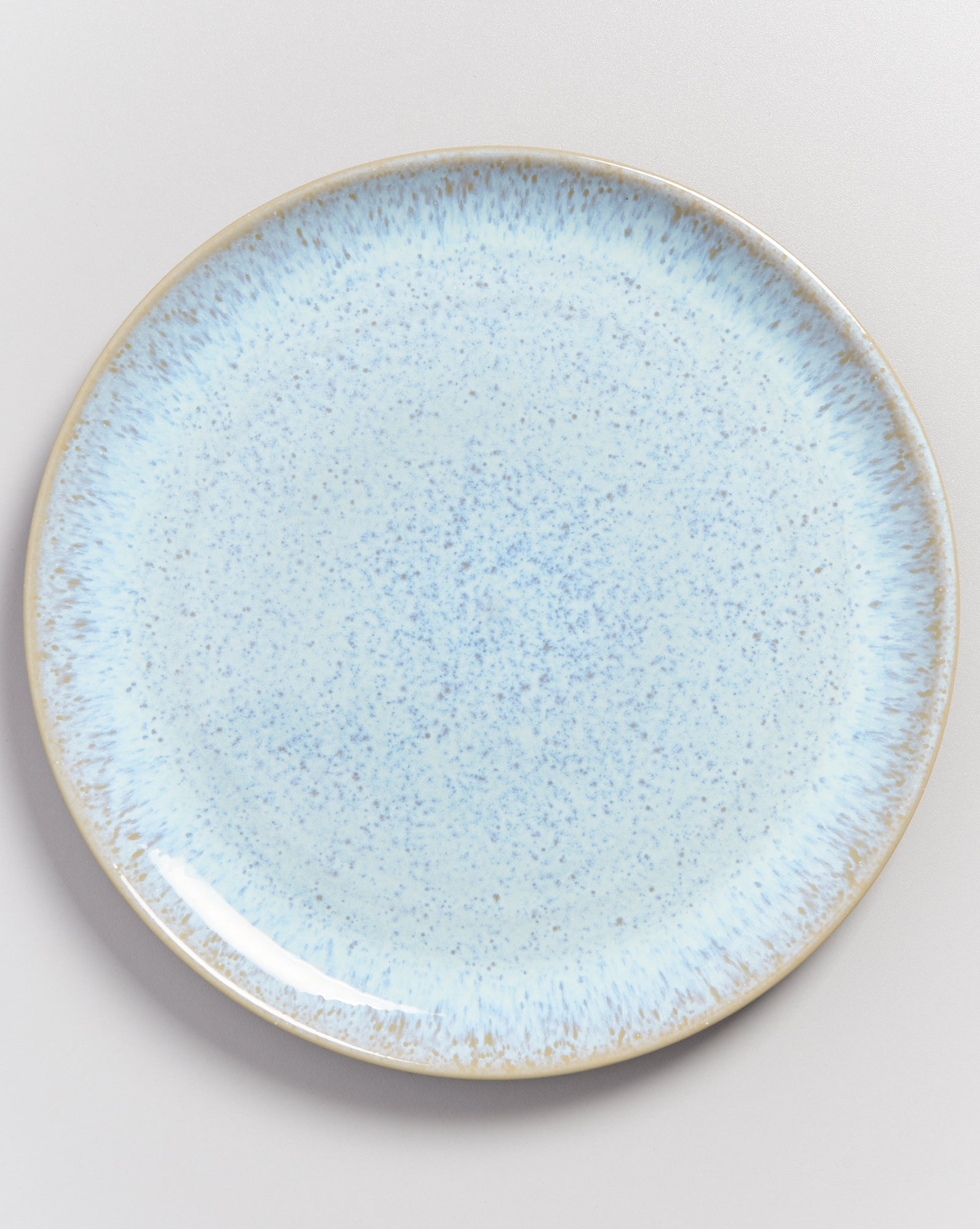 Runder Teller mit blau-weißer Sprenkel- und Glanzoptik auf einem hellgrauen Hintergrund.