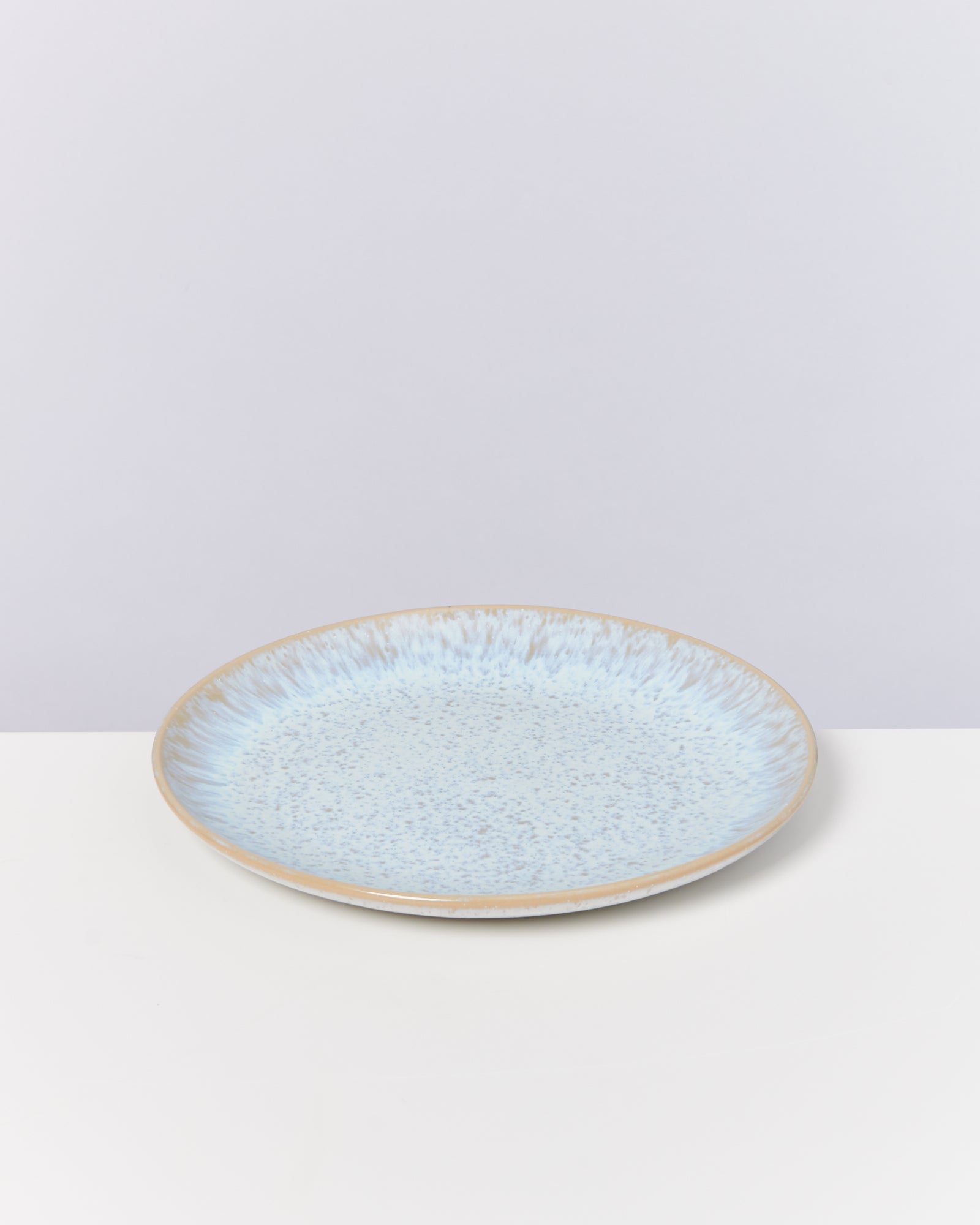 Ein flacher, heller Teller mit bläulich gesprenkeltem Muster auf weißem Hintergrund.