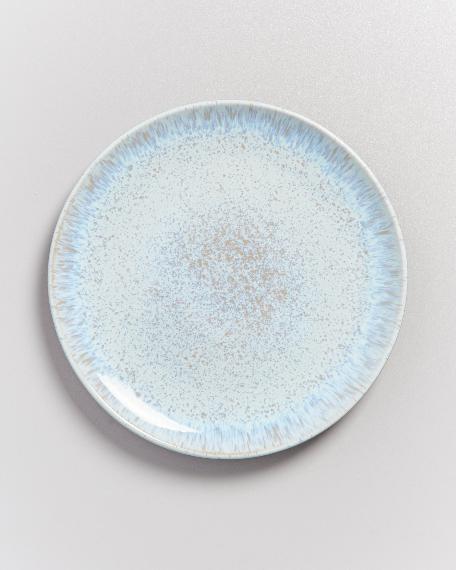 Runder Teller mit blauen und braunen Sprenkeln auf weißem Hintergrund.