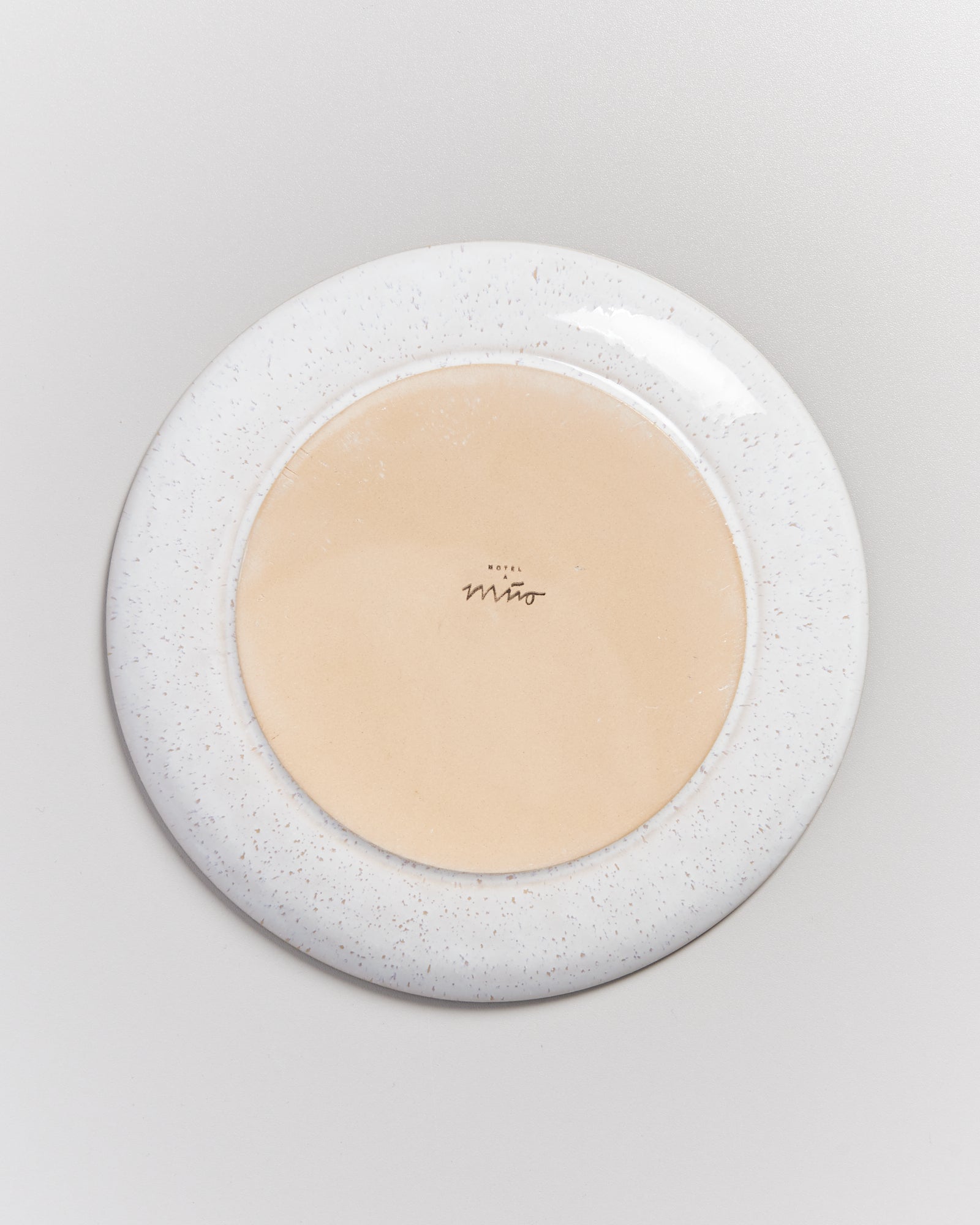 Rückseite eines runden, gesprenkelten Tellers mit der Aufschrift "Hotel Miro" auf hellem Untergrund.