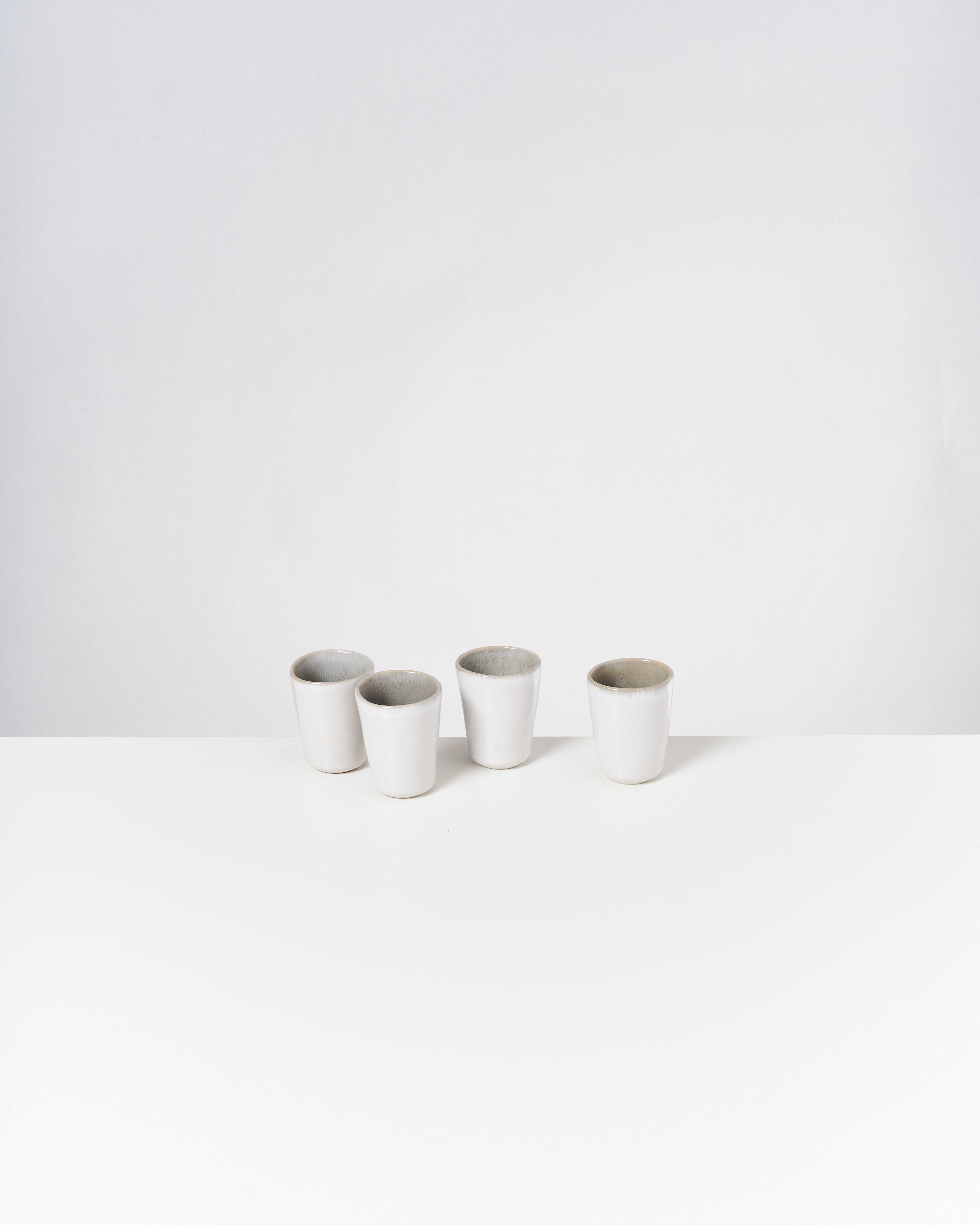 Vier weiße Keramiktassen auf einem weißen Tisch vor neutralem Hintergrund.