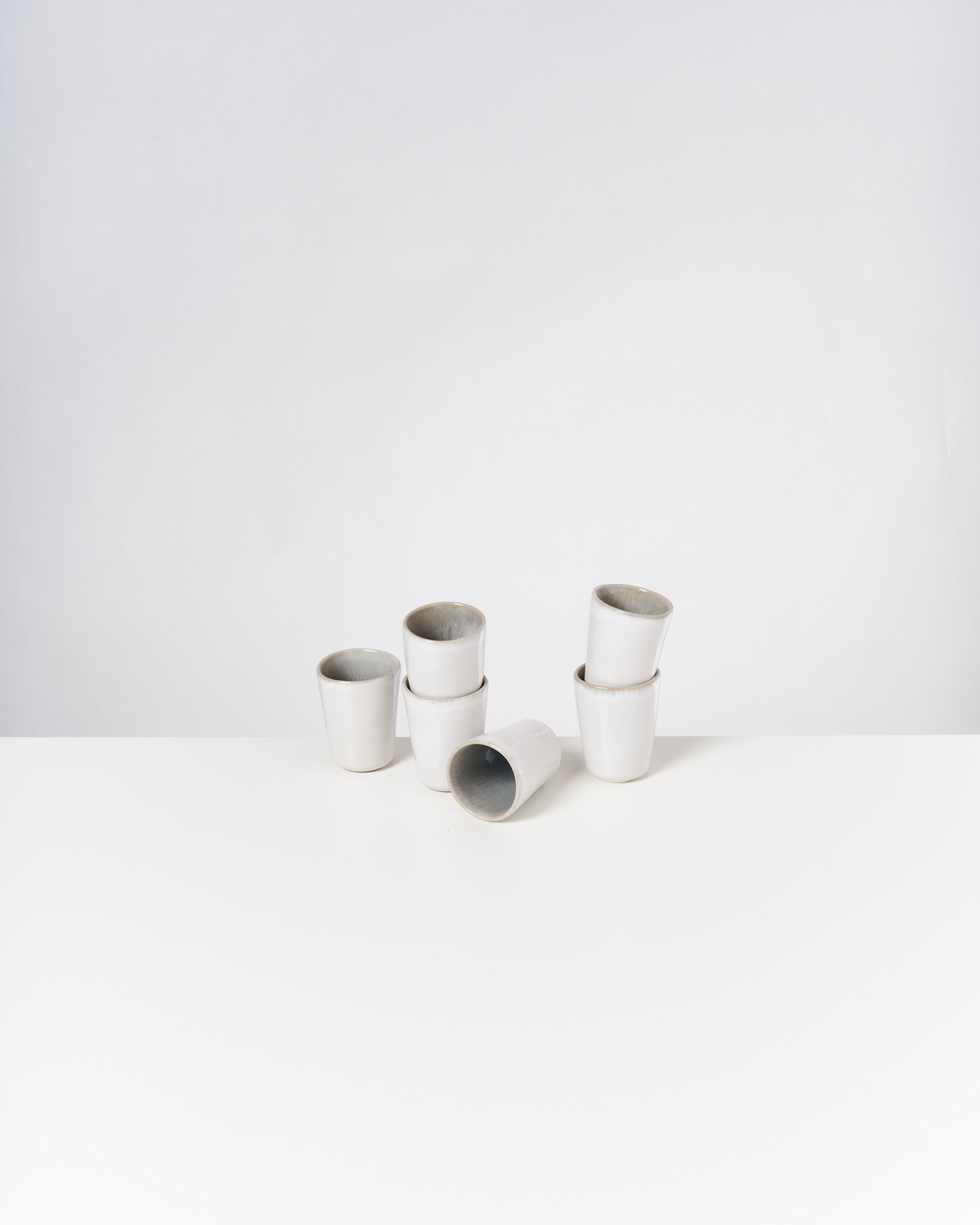 Sechs weiße Keramikbecher stehen gestapelt auf einem weißen Tisch, einer liegt auf der Seite.