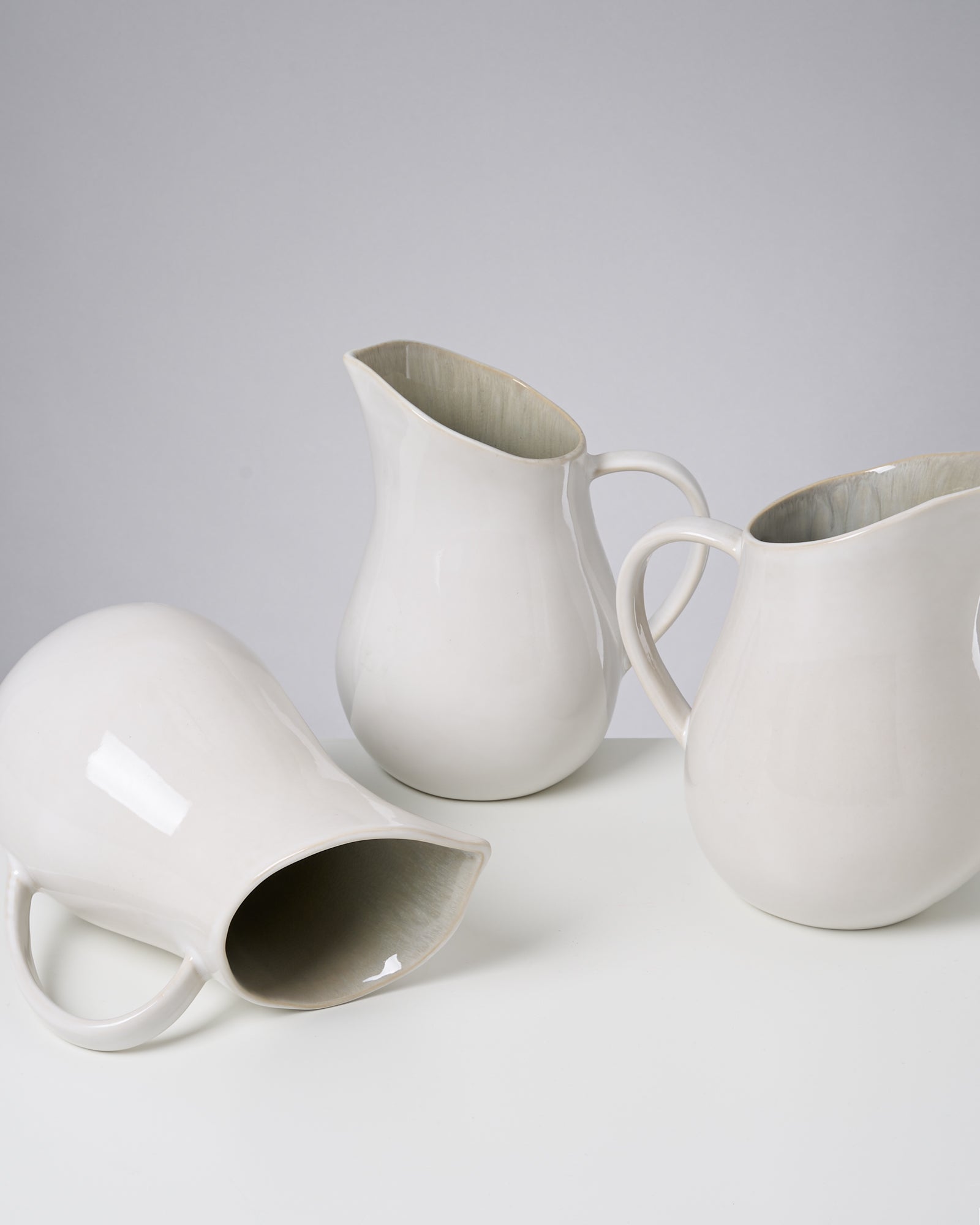 Drei weiße Keramikkrüge, zwei stehend und einer liegend auf einem weißen Untergrund.
