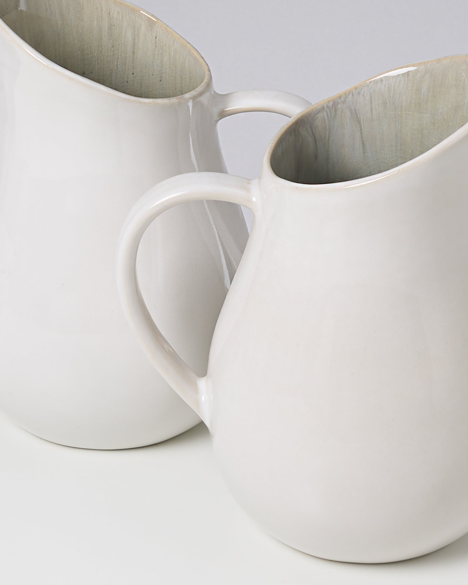 Zwei weiße Keramikkrüge mit gebogenen Henkeln stehen nebeneinander auf einem weißen Hintergrund.