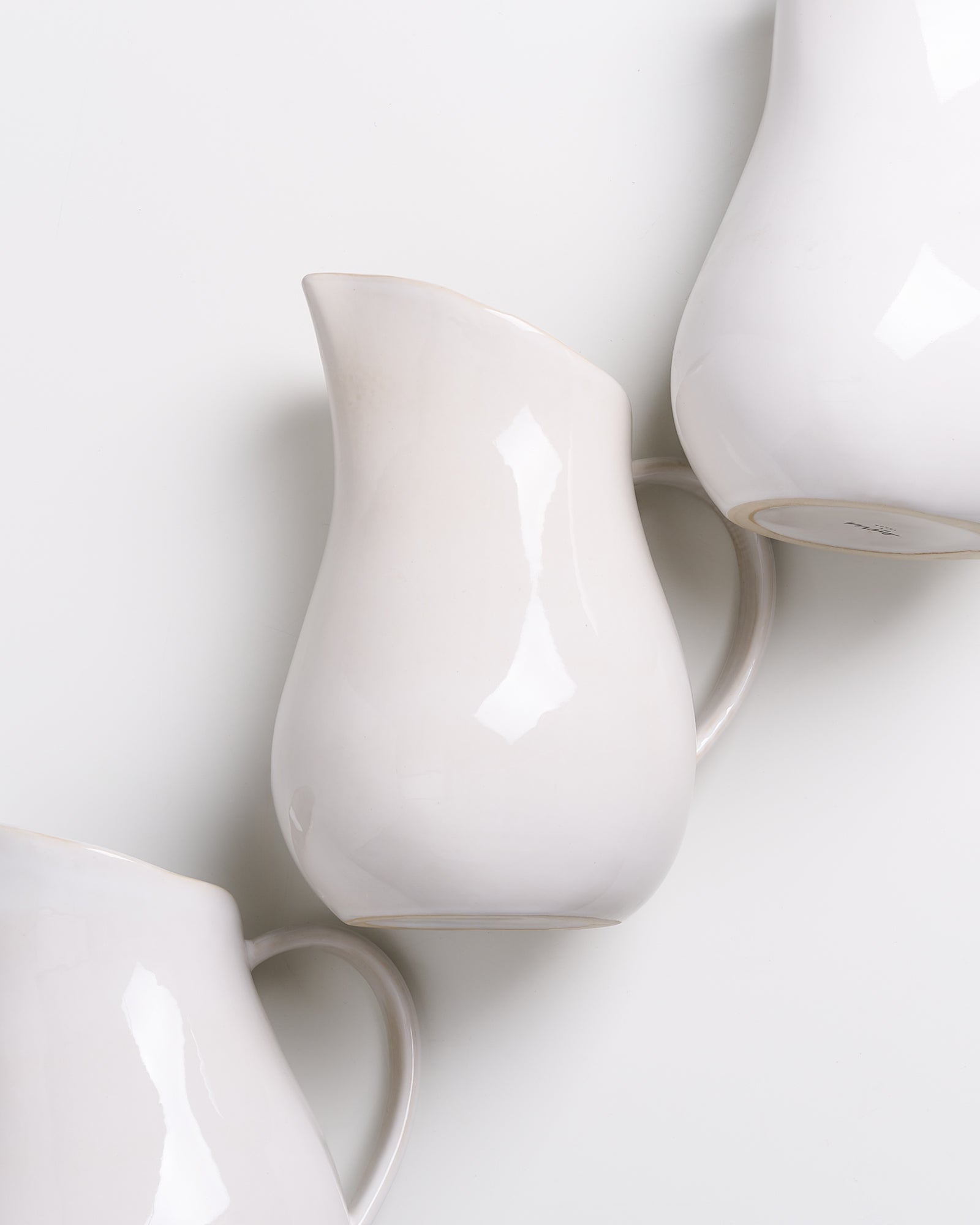 Drei weiße, glänzende Krüge stehen diagonal auf einer weißen Oberfläche.