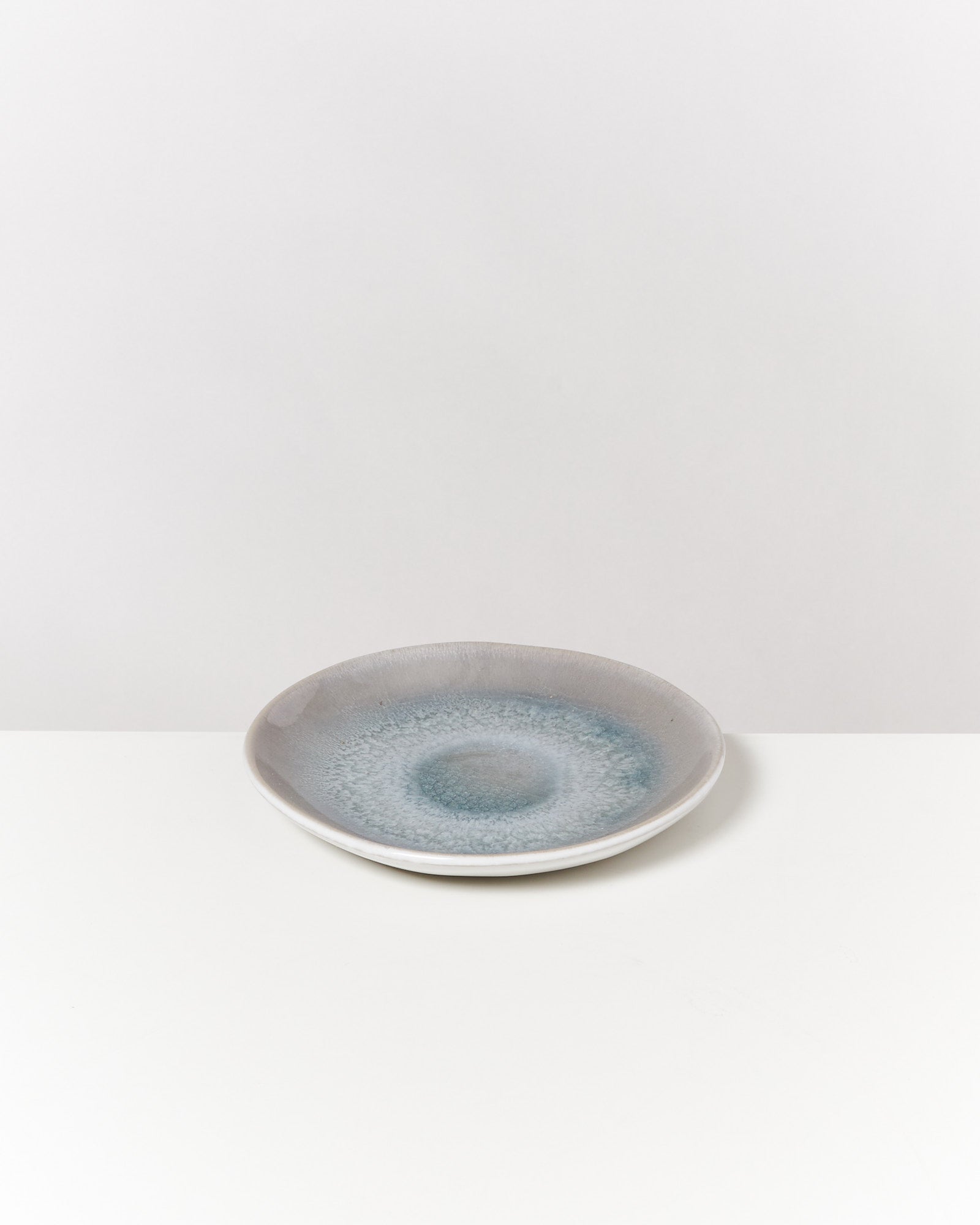 Grauer Teller mit bläulichem Muster auf weißem Hintergrund.
