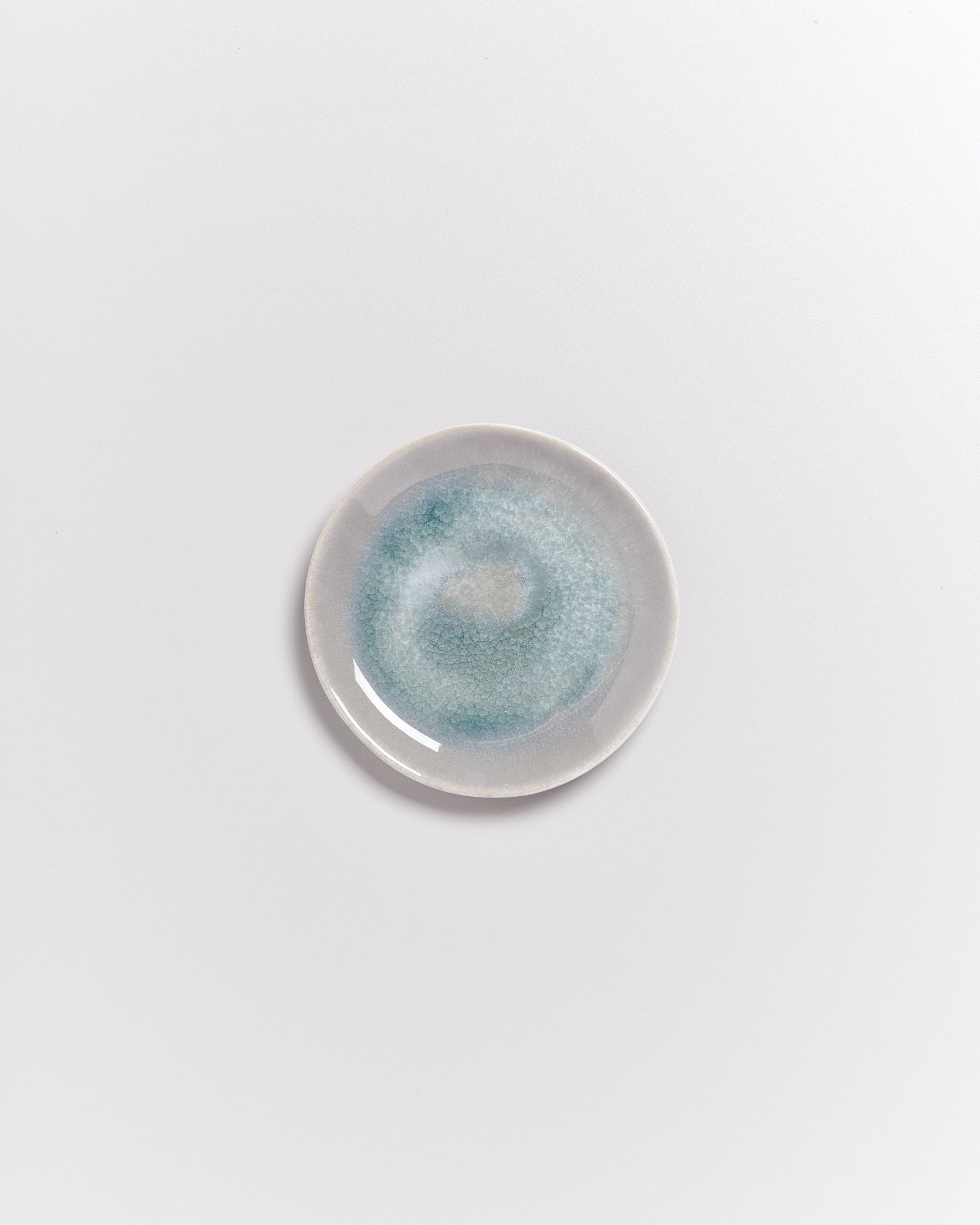 Kleiner Keramikteller mit blau-grüner Glasur auf weißem Hintergrund.