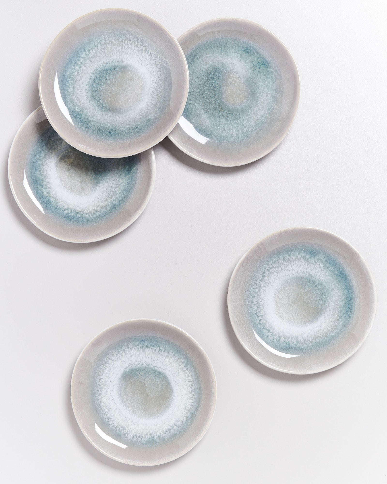 Fünf runde Teller mit blau-grauem, kreisförmigem Muster liegen auf weißem Hintergrund.