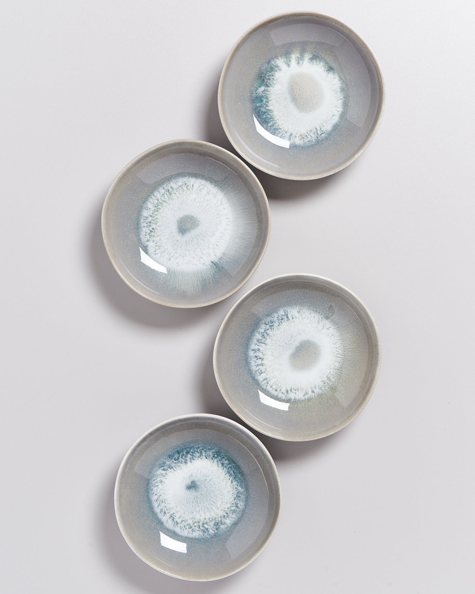 Vier runde, graue Teller mit blau-weißen, kreisförmigen Mustern auf hellem Hintergrund.