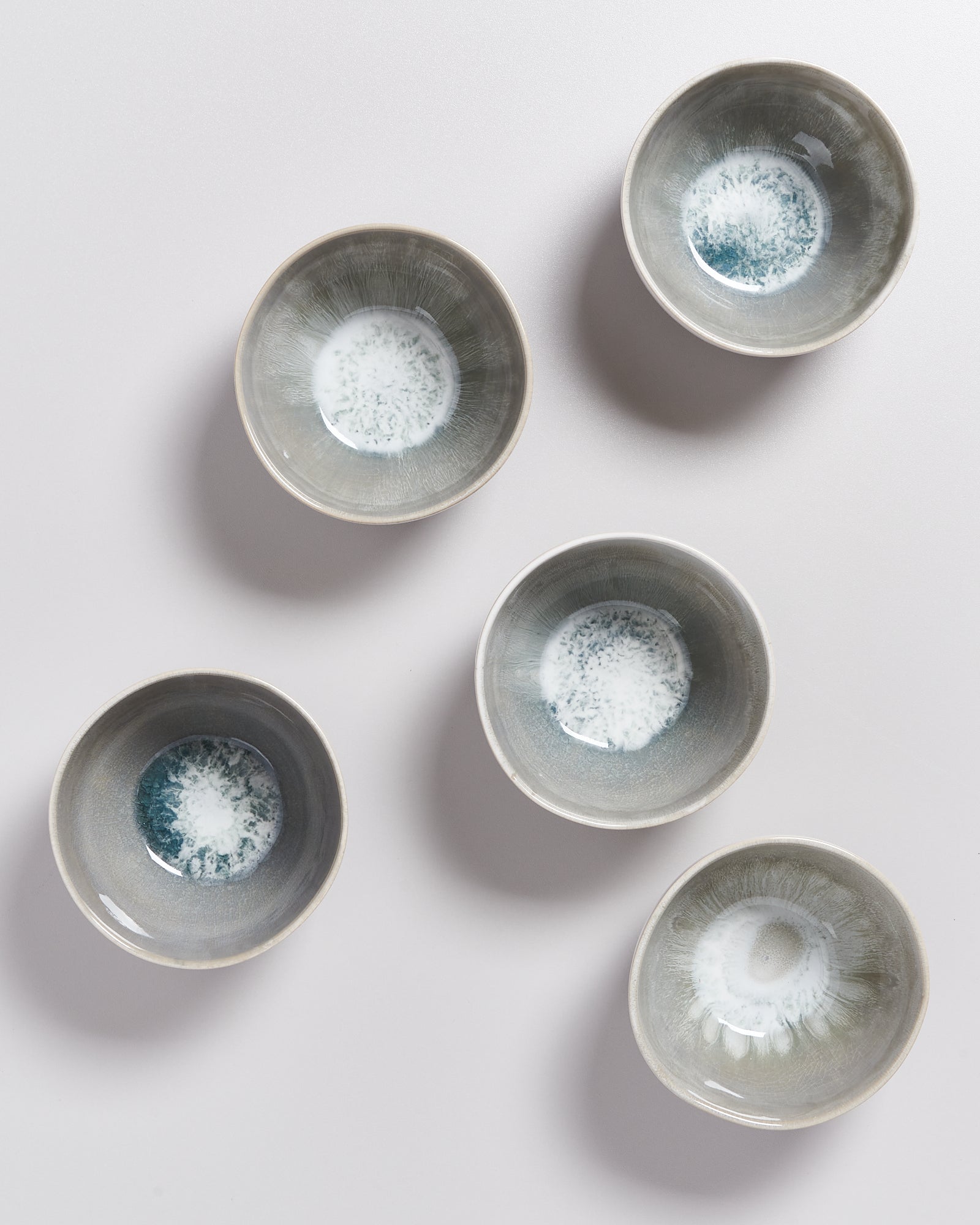 Fünf graue Keramikschalen mit weißen und blauen Mustern im Inneren liegen auf einem hellen Untergrund.