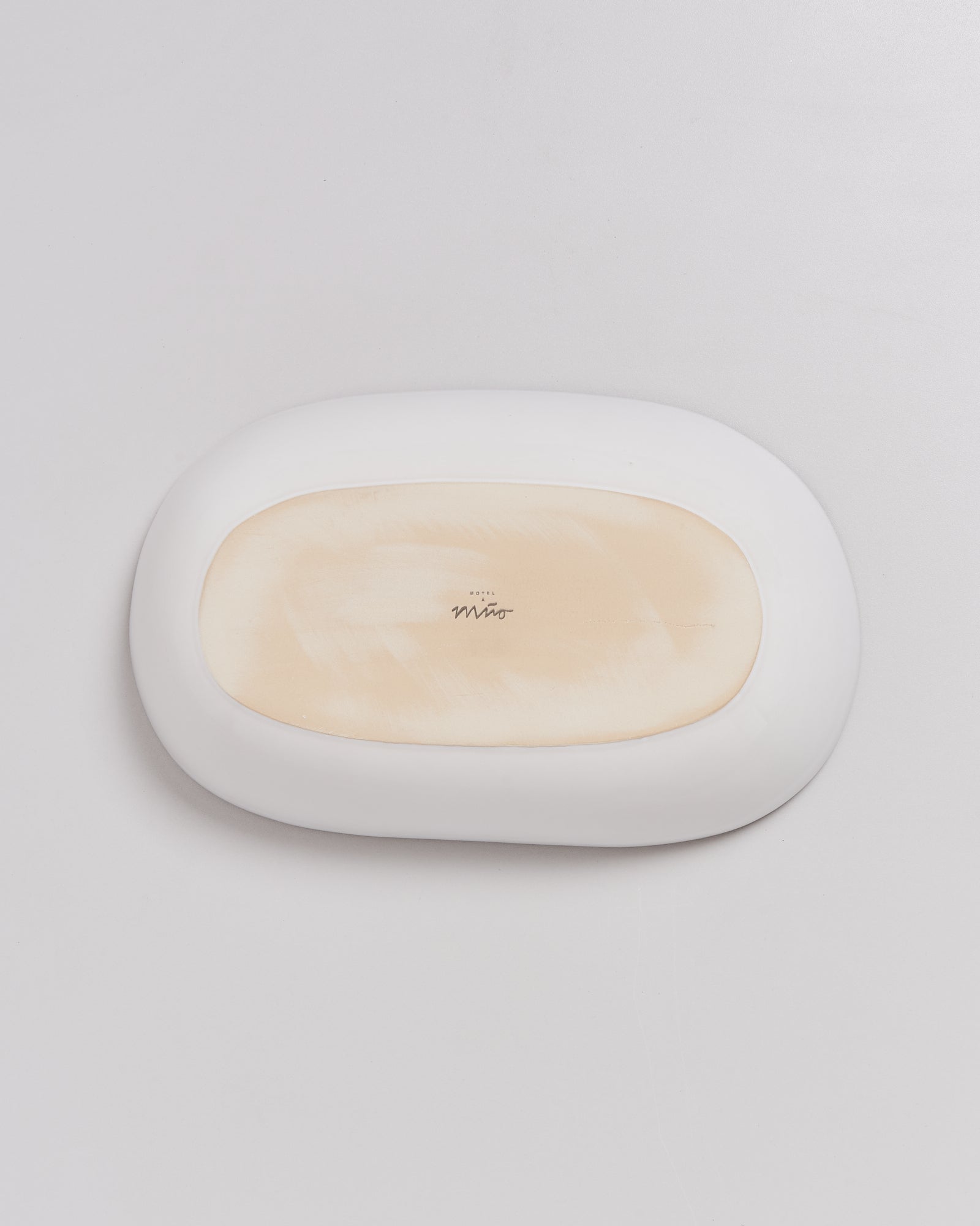 Ovaler, weißer Stein mit beiger Oberseite und einer Signatur in der Mitte auf grauem Hintergrund.