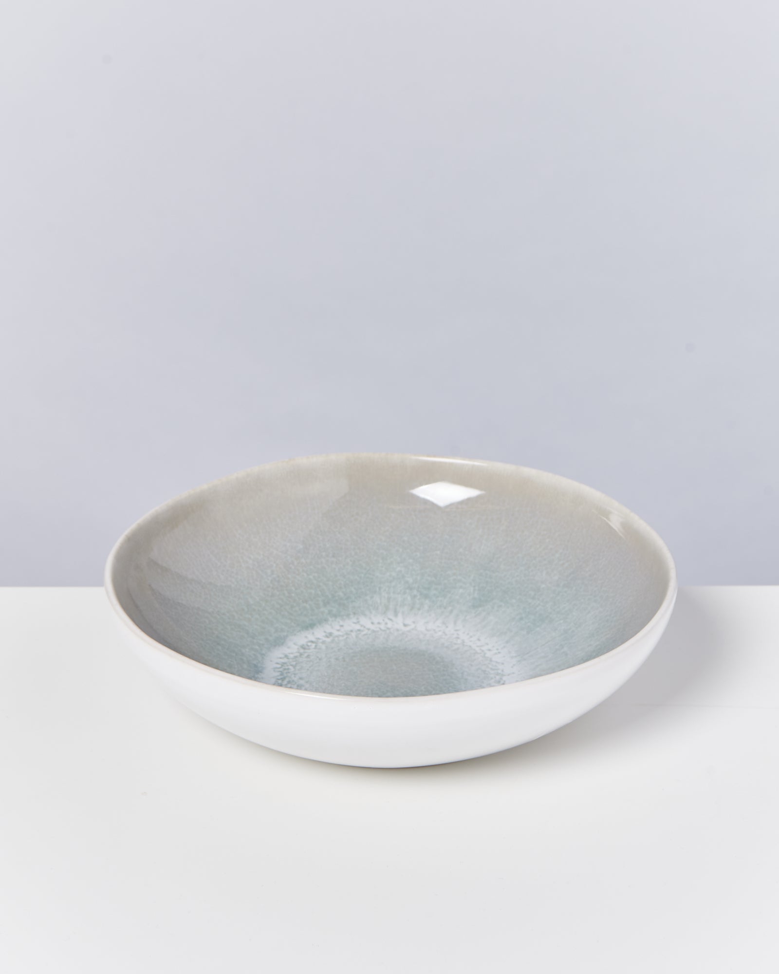 Keramikschüssel mit blau-grauem Verlauf, auf einem weißen Untergrund vor grauem Hintergrund.