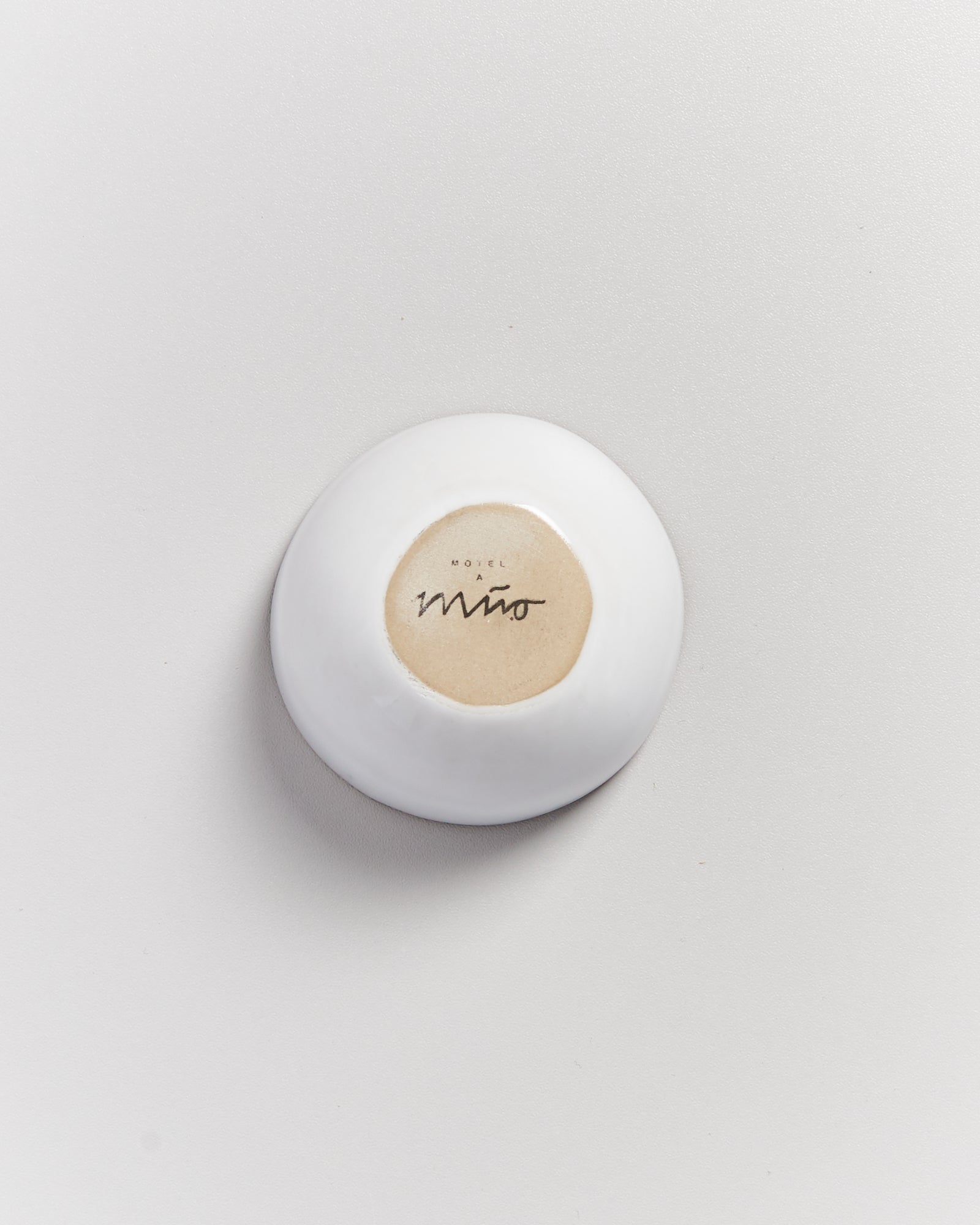 Weiße Schale mit dem Schriftzug "Hotel a Mino" auf beigem Boden, auf einem hellen Hintergrund.